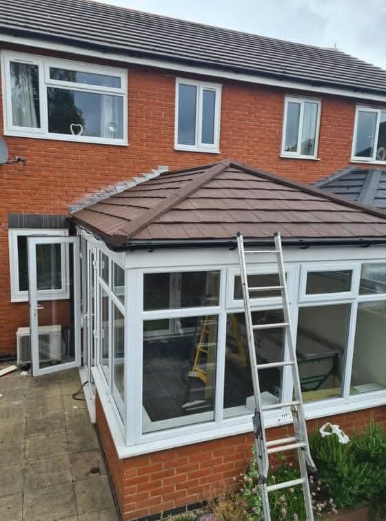 Brown tiled conservatory roof on white uPVC conservatory extension with ladder against wall
