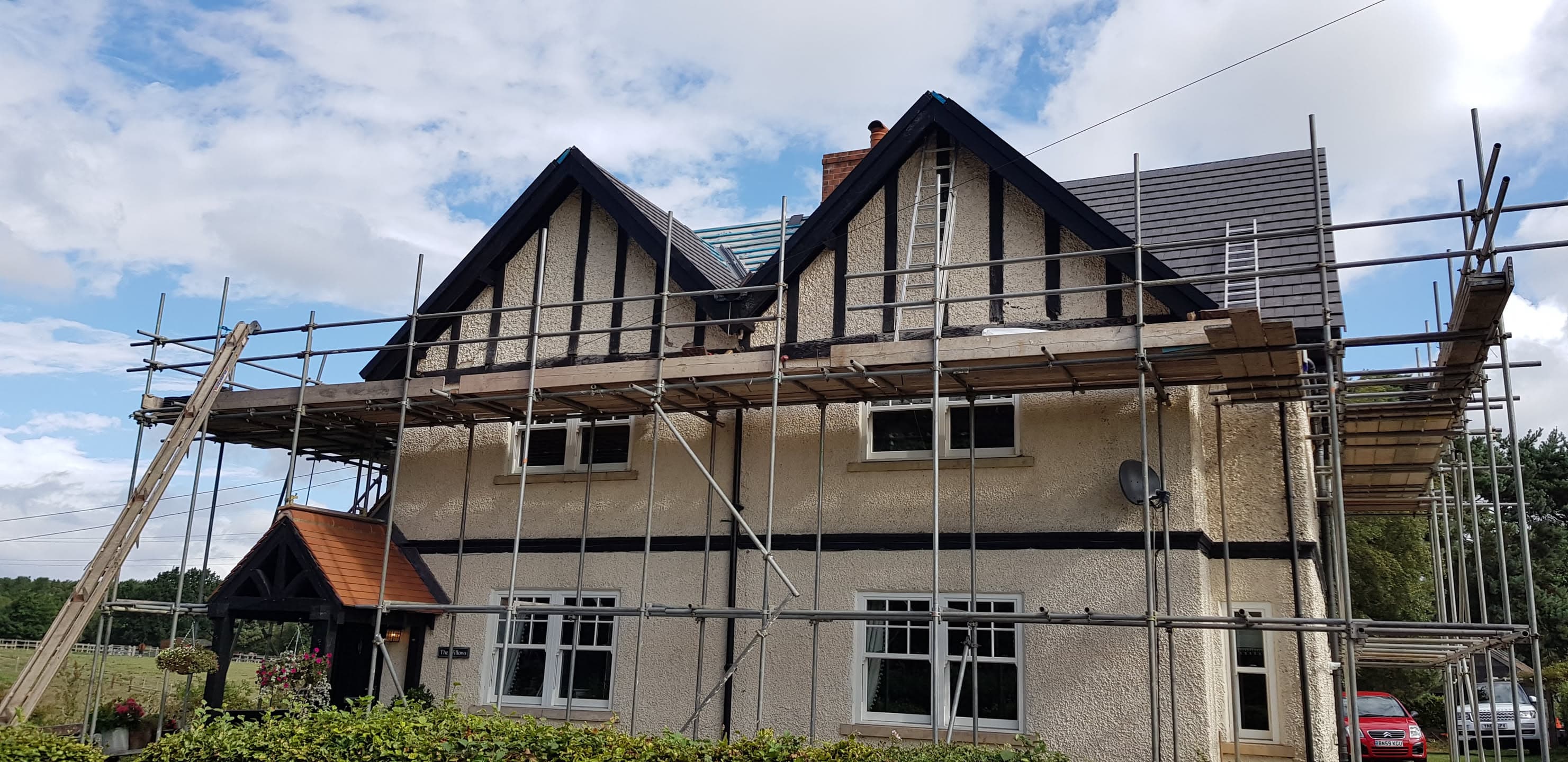 Pitched roof with grey concrete tiles and mock Tudor gable details, scaffolding erected around property