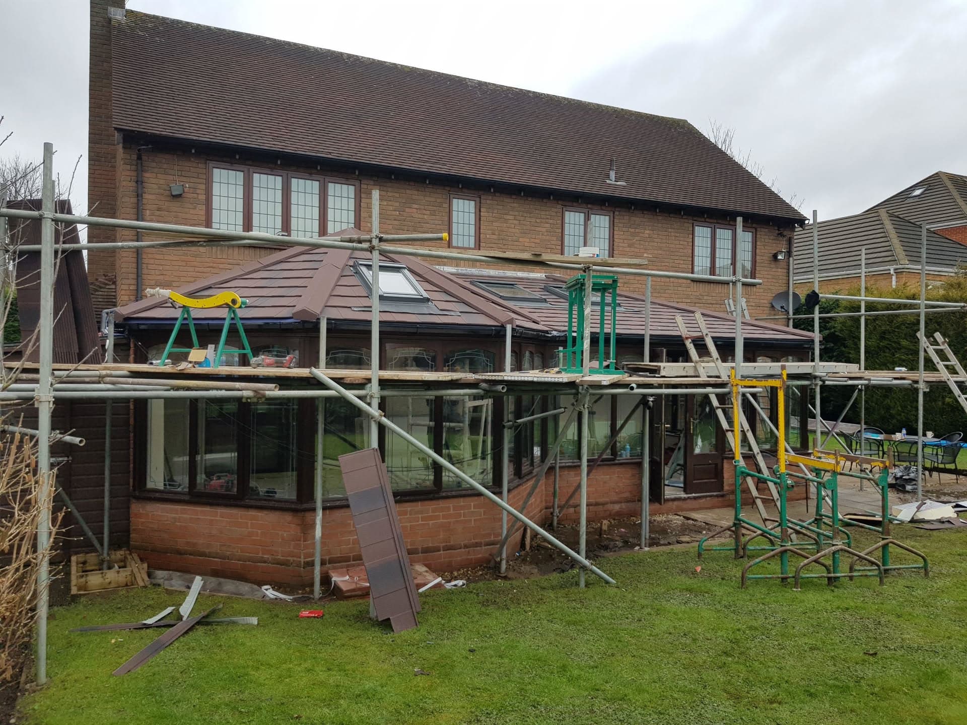 Brown metal conservatory roof installation with scaffolding on brick house