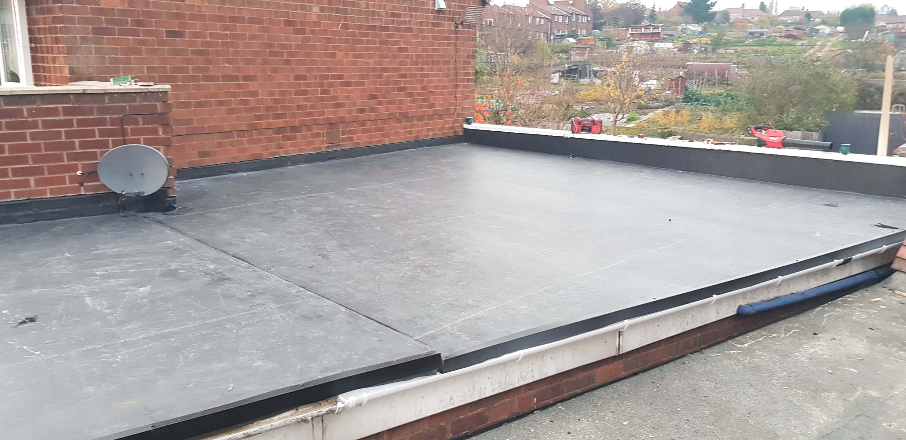 Completed grey EPDM rubber flat roof with black trim against brick wall