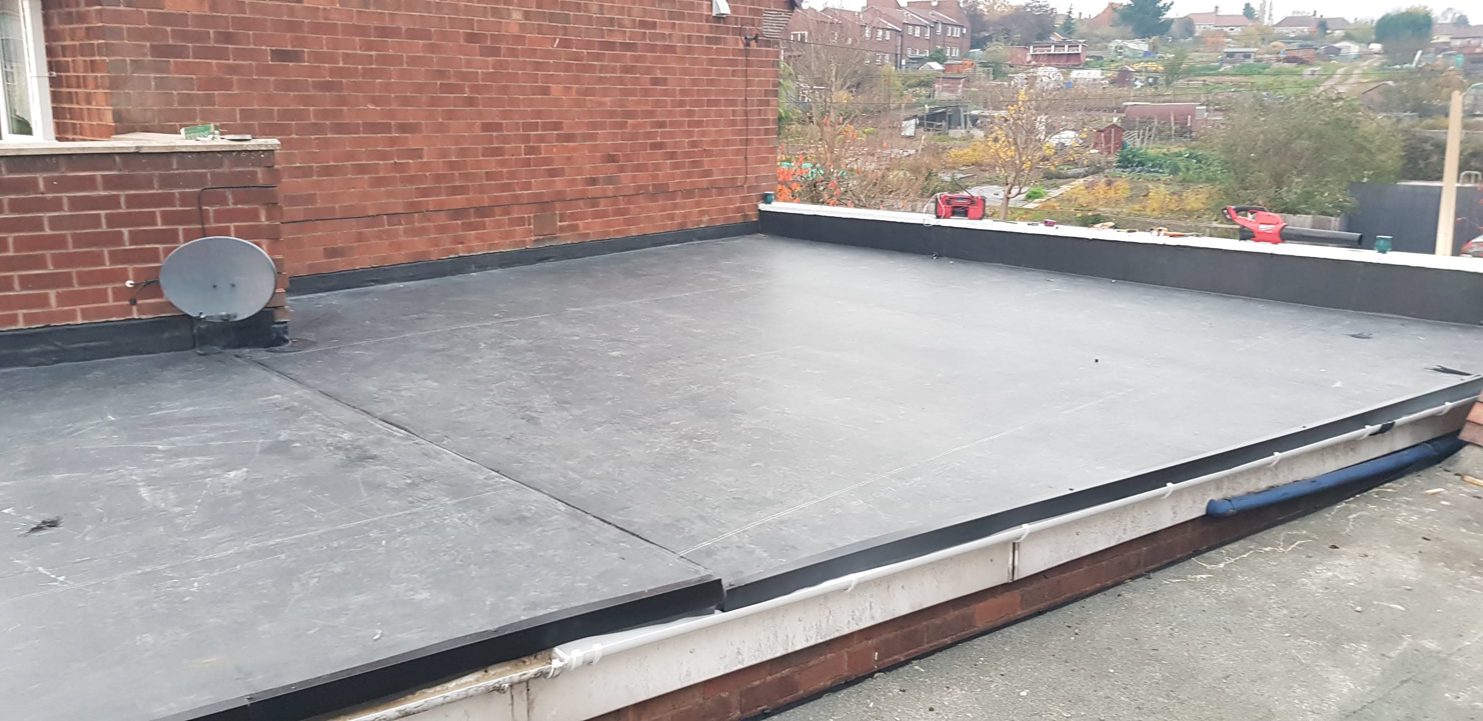 Completed grey EPDM rubber flat roof with black trim against brick wall