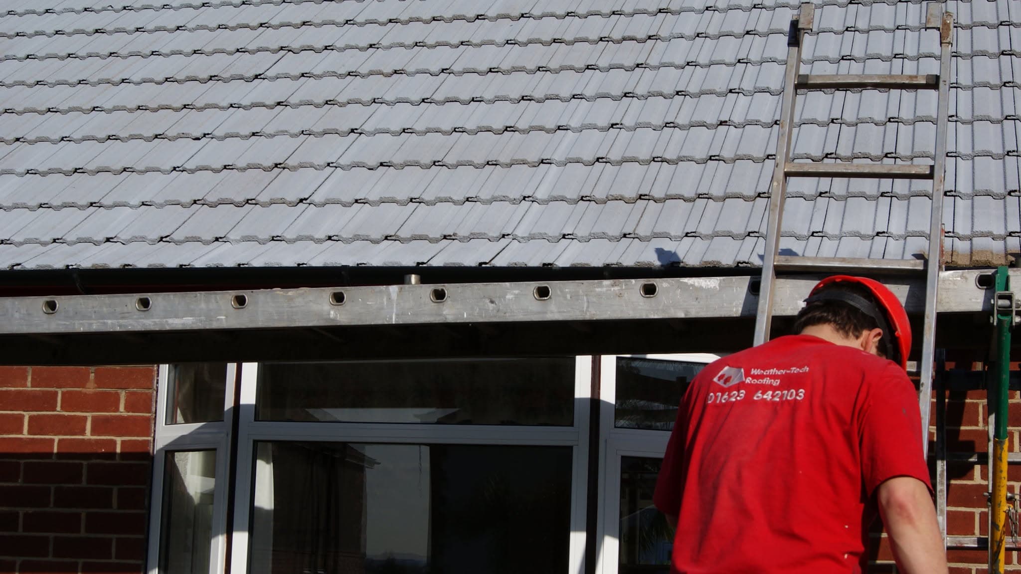 WeatherTech fitter working on grey concrete tiled pitched roof with fascia board and ladder