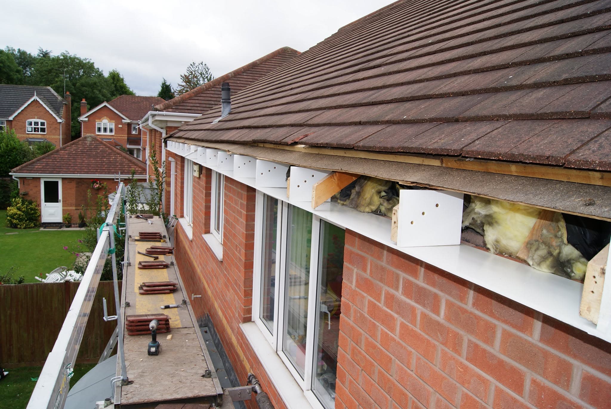 Pitched concrete tiled roof with damaged fascia and exposed roof timbers during repair work