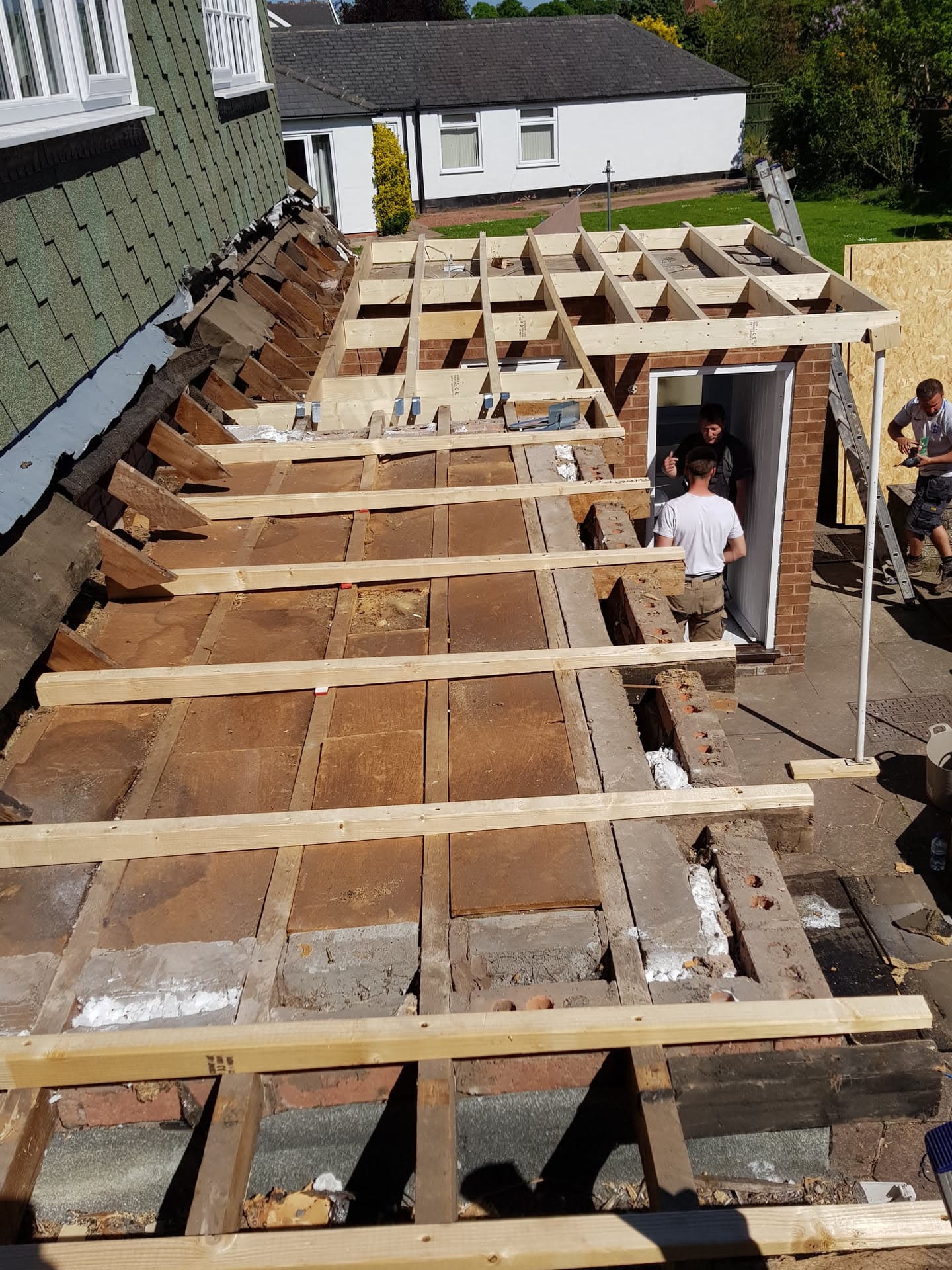 Flat roof extension under construction with exposed timber joists and fitters working