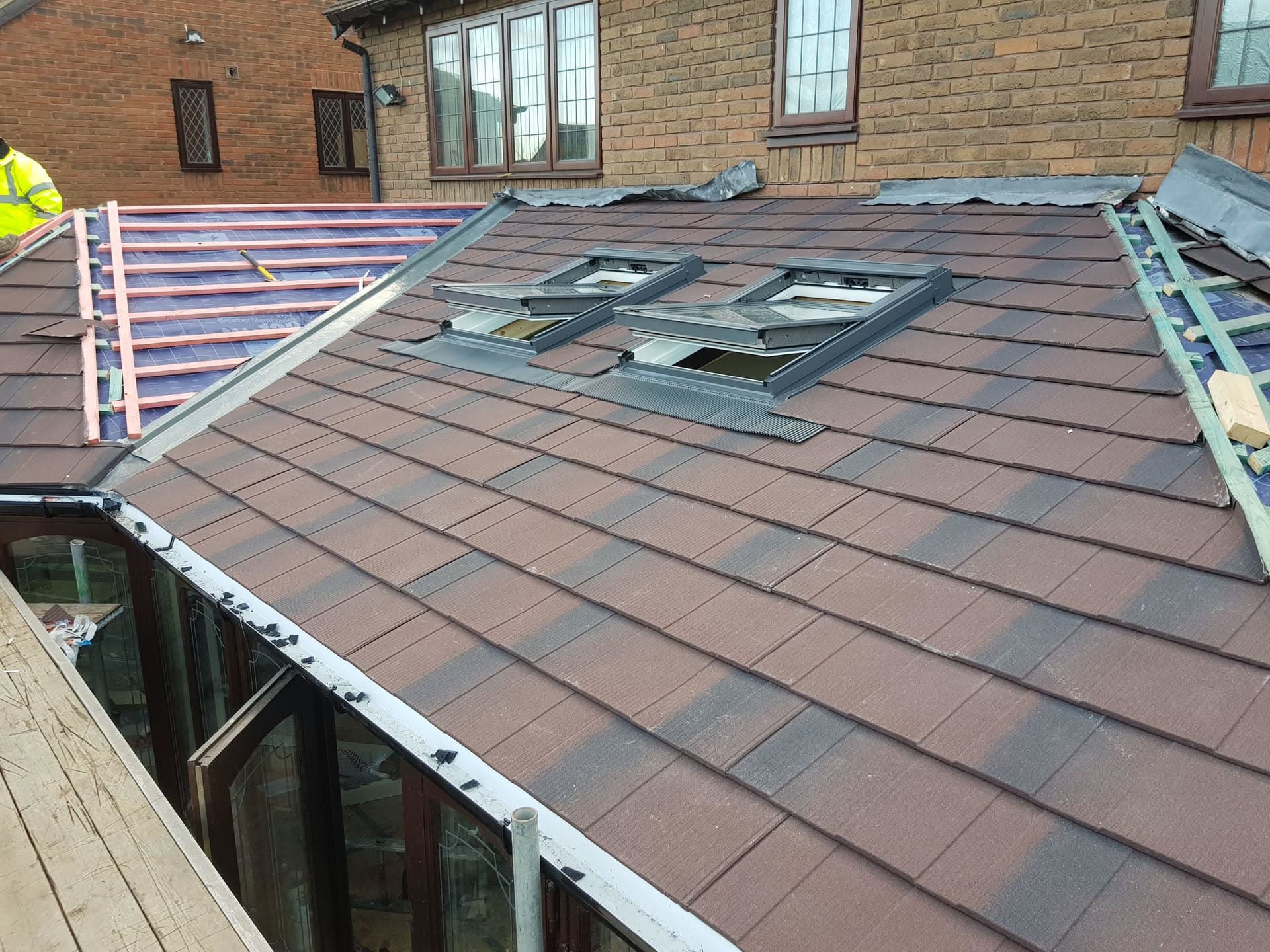 Pitched roof with brown concrete tiles and two grey metal roof windows during installation