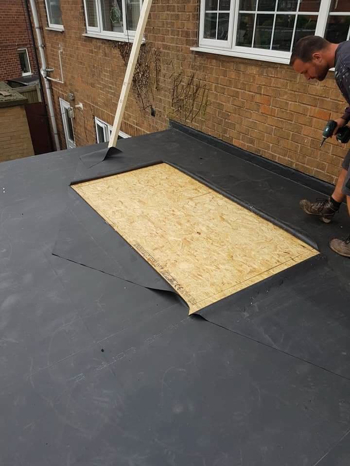 Flat roof installation in progress with dark grey felt membrane and OSB board visible, fitter working
