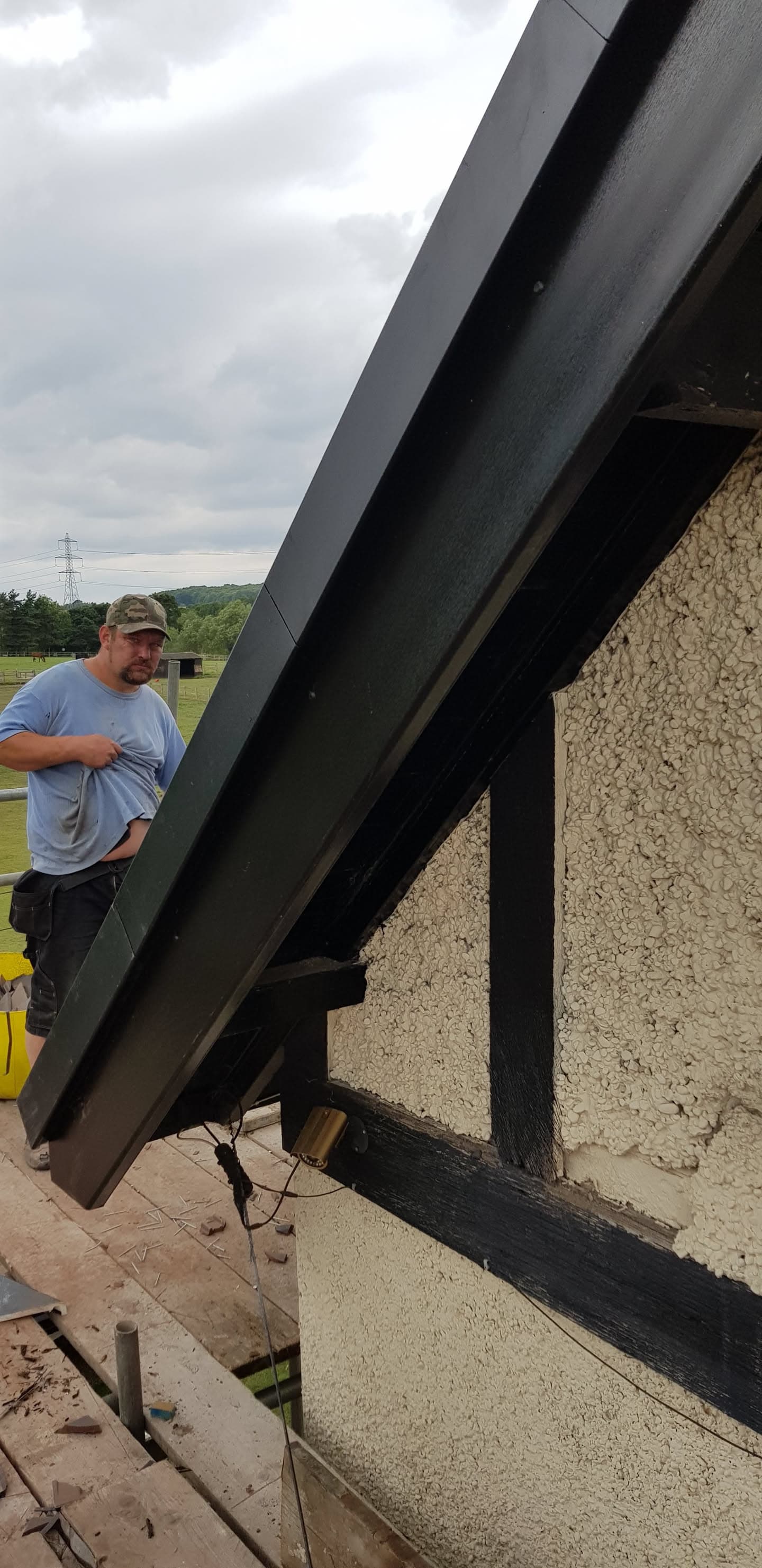 Fitter installing dark grey fascia board on pitched roof edge