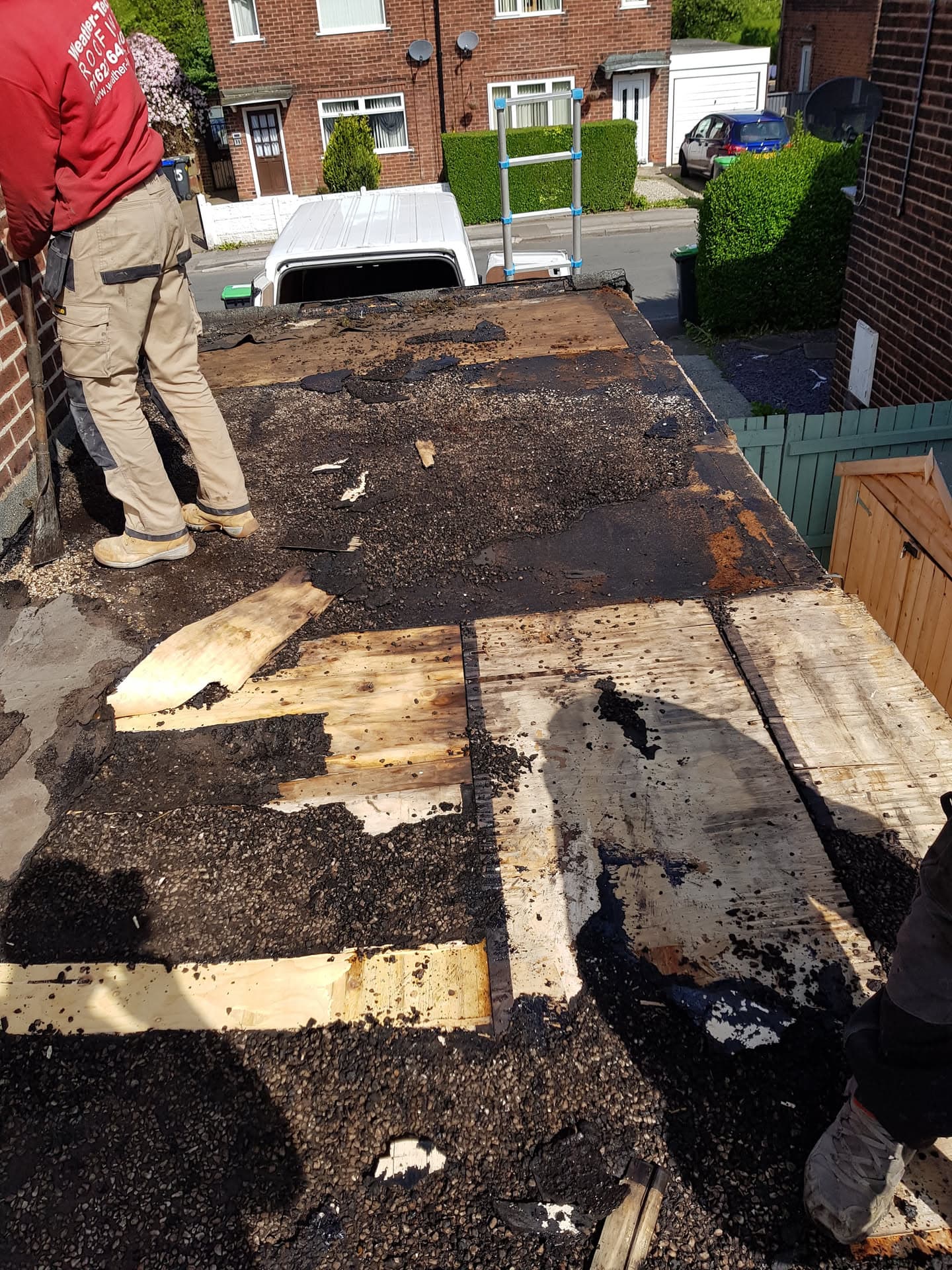 Flat roof with old felt being stripped away, exposing timber decking beneath, fitter standing at edge