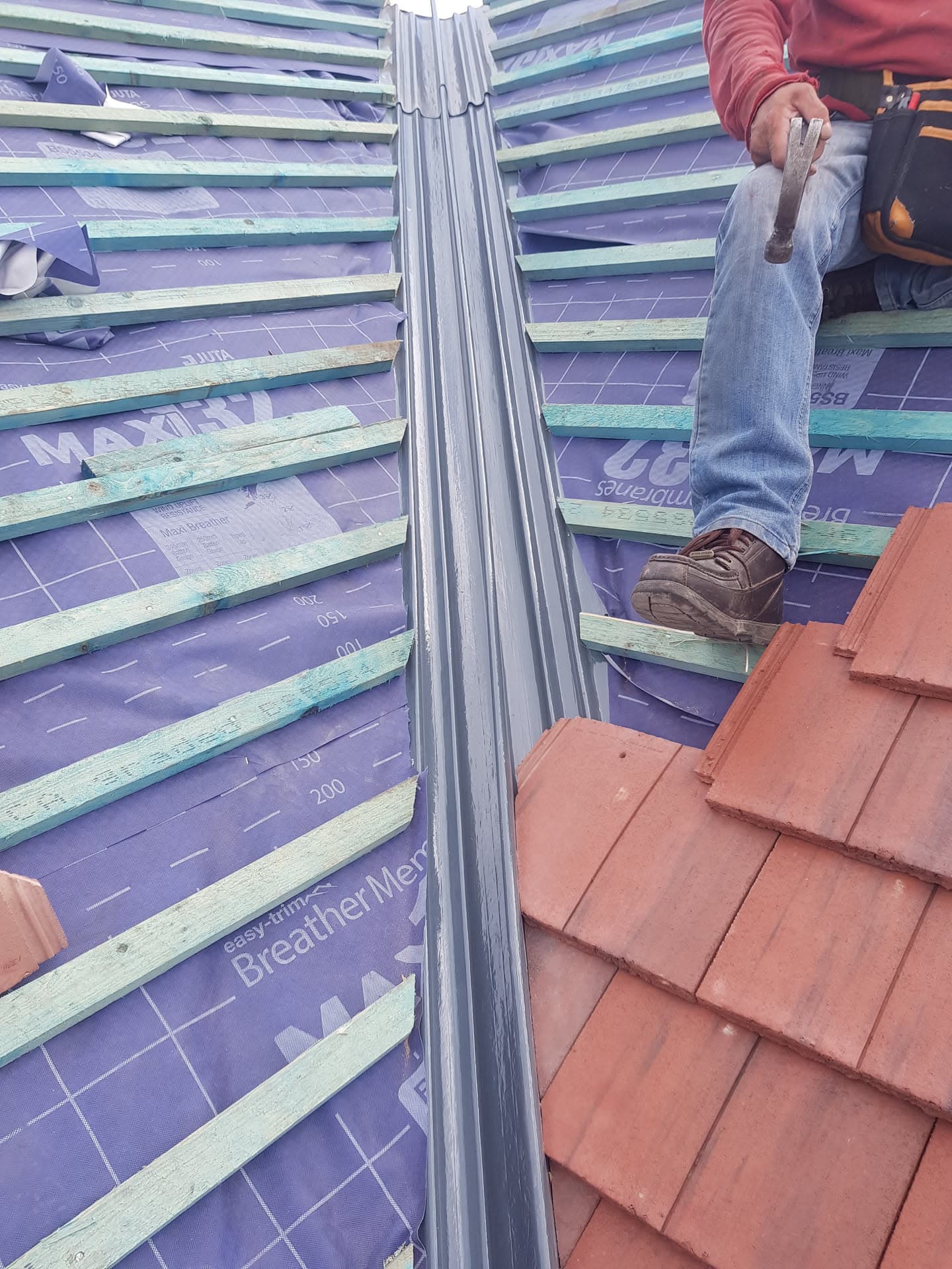 Roofer installing terracotta tiles on pitched roof with battens and breathable membrane visible
