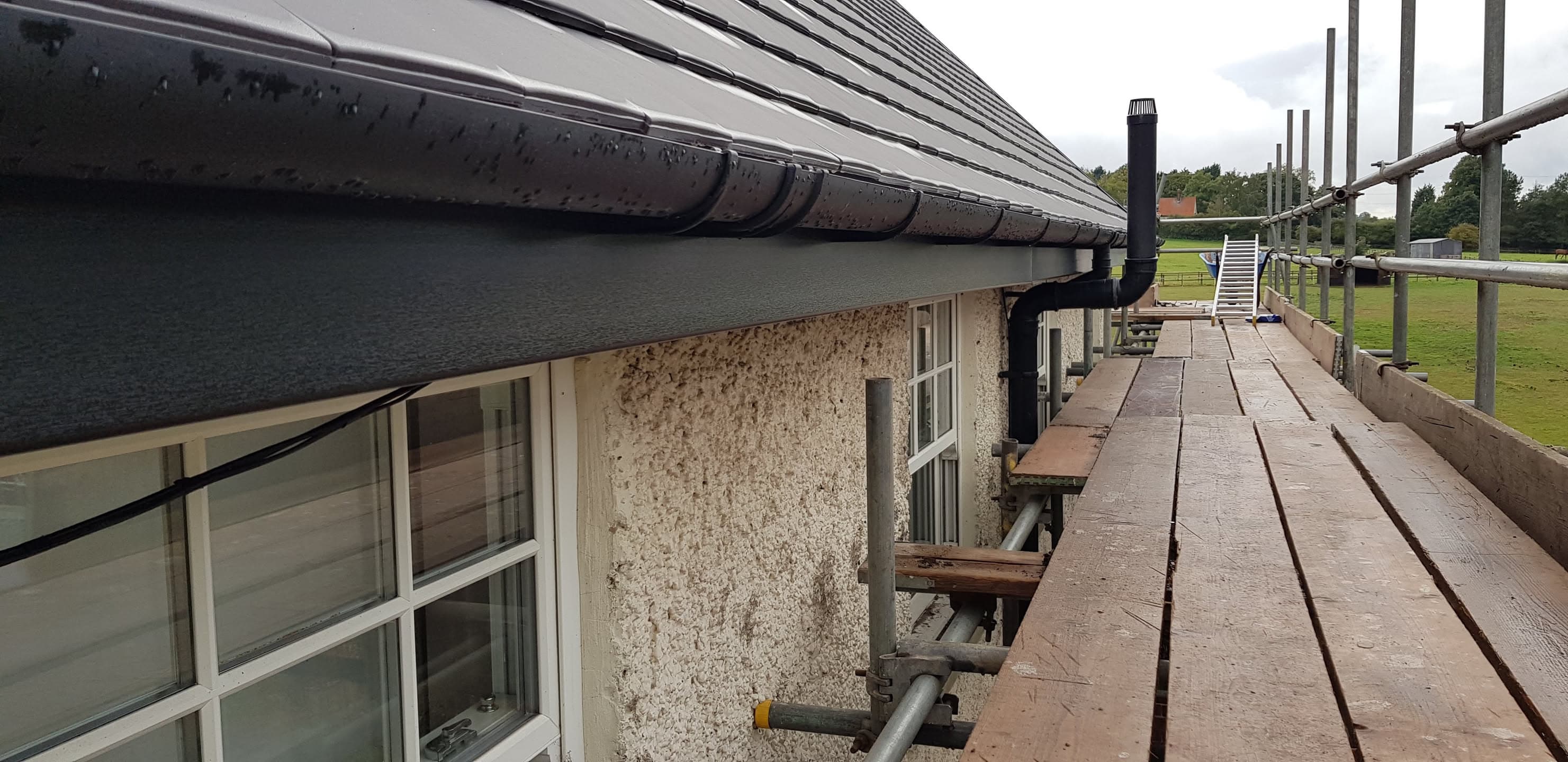 Black guttering and fascia board on pitched roof with scaffolding platform
