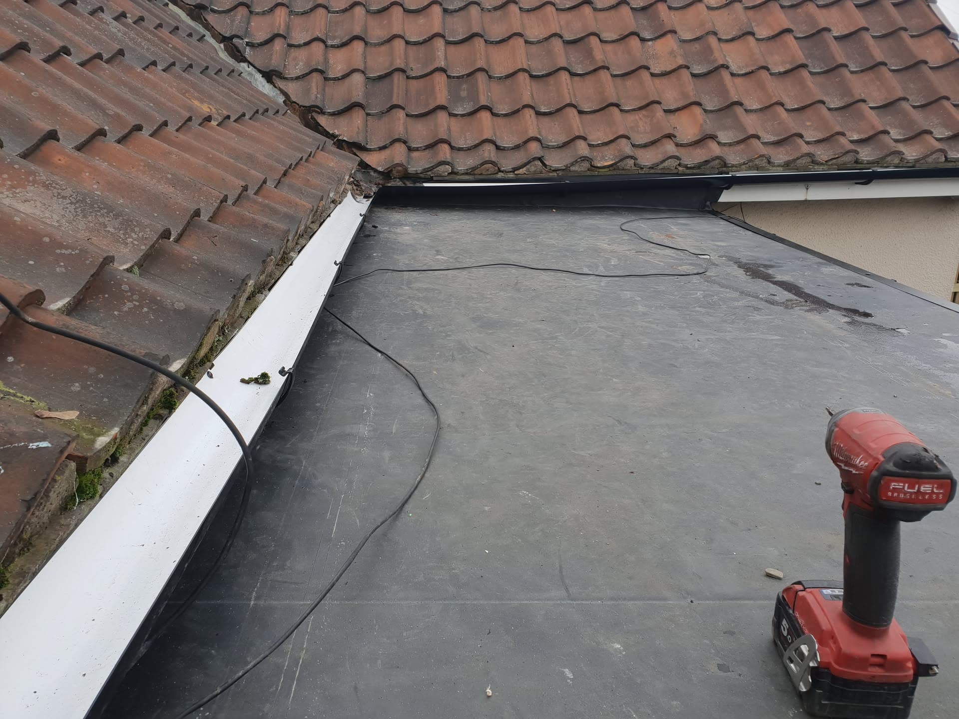 Flat roof with EPDM rubber membrane and white fascia trim alongside brown concrete tiled pitched roof