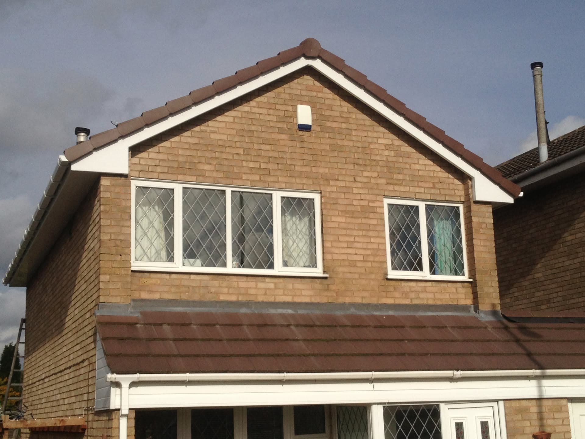 Pitched roof with red concrete tiles and white fascias and guttering on brick house