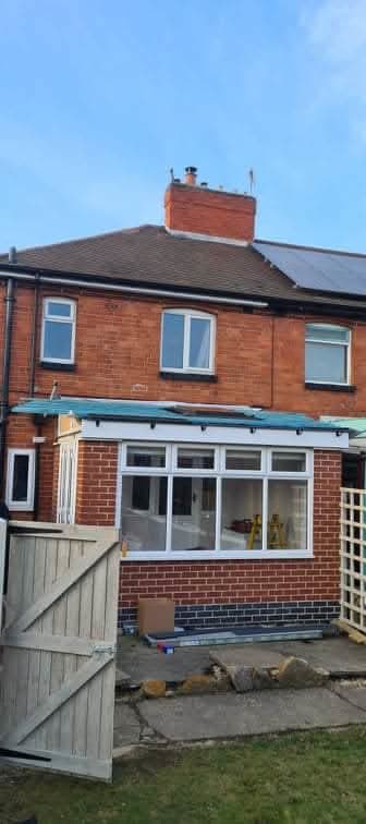 Red brick terraced house with grey tiled pitched roof and white conservatory extension