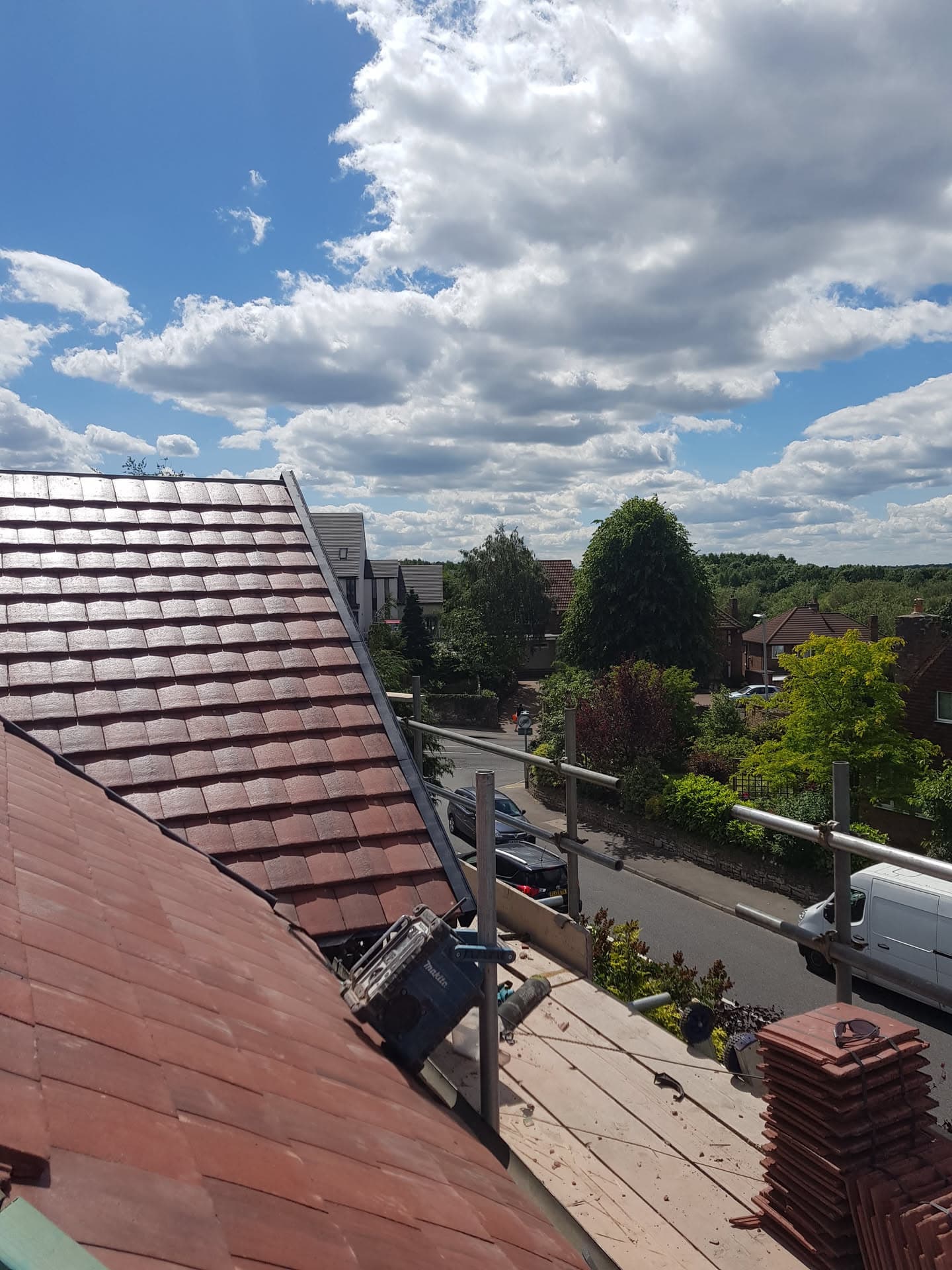 Pitched roof with red concrete tiles and ridge scaffolding overlooking residential street