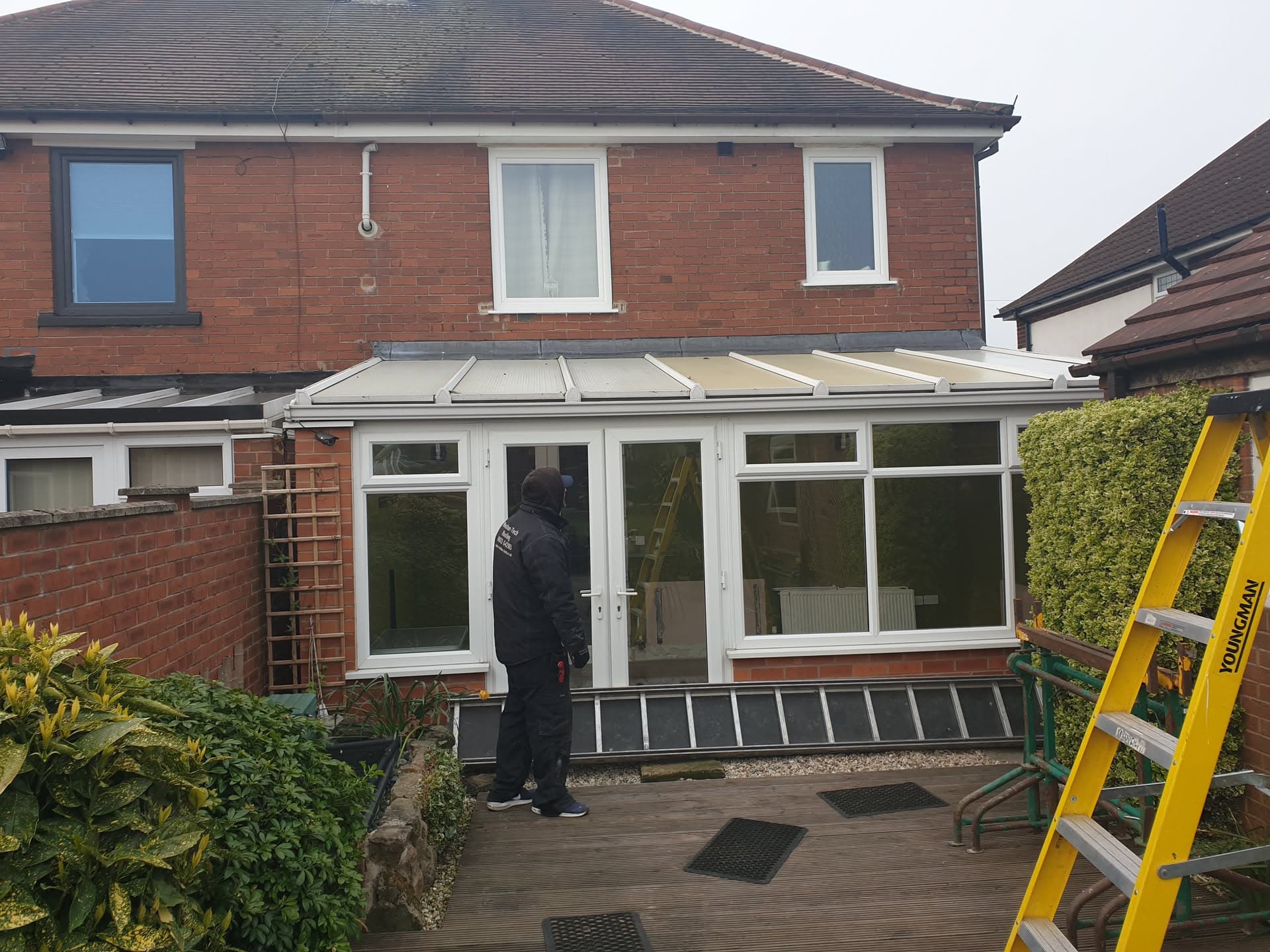 Conservatory with cream flat roof panels and white uPVC frames, fitter working at rear door