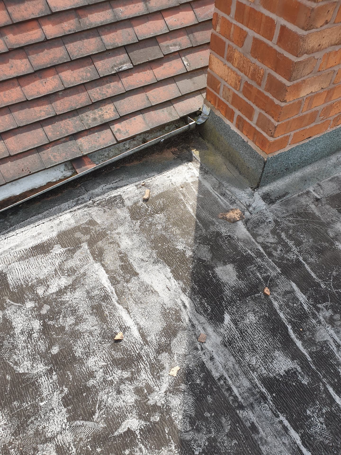 Flat roof with grey felt surface meeting tiled pitched roof and brick chimney stack