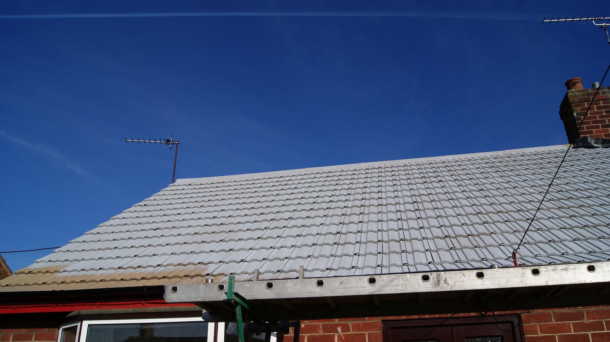 Pitched roof with grey concrete tiles and brick chimney stack against clear blue sky