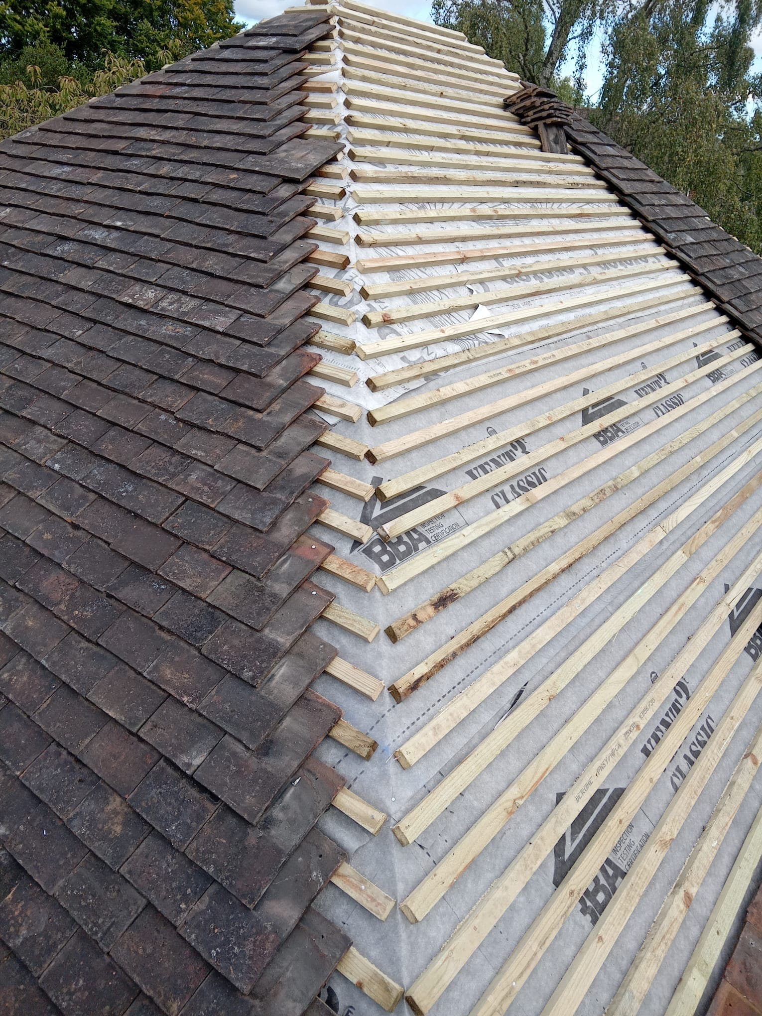 Hipped roof half re-tiled, with breathable membrane and new timber battens exposed alongside reclaimed clay plain tiles