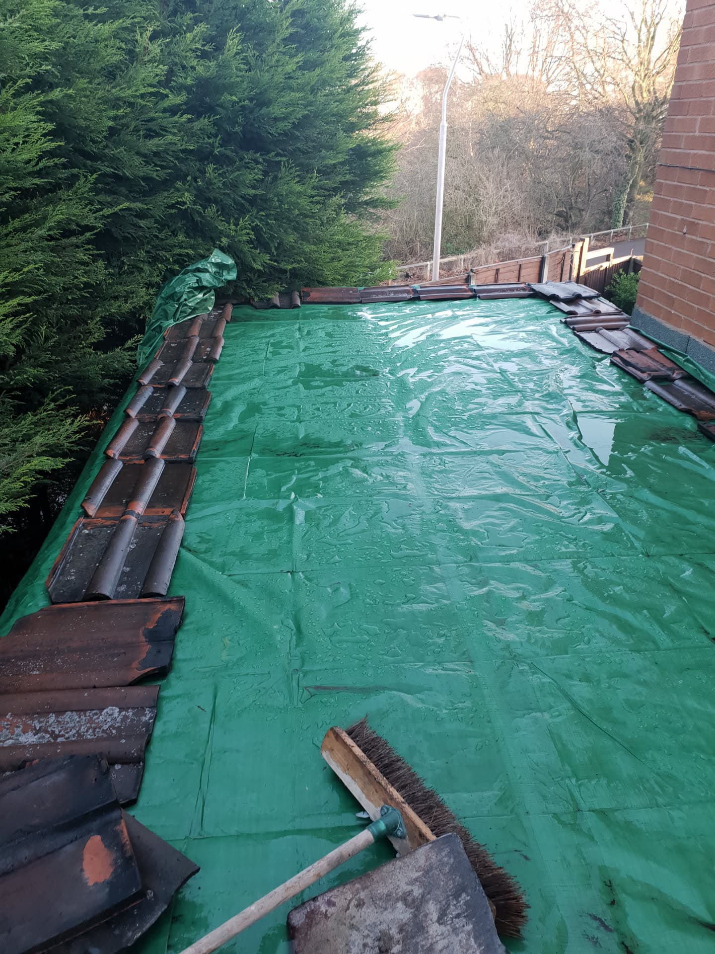 Flat roof covered with green protective membrane during re-roofing work with brown concrete tiles stacked at edges