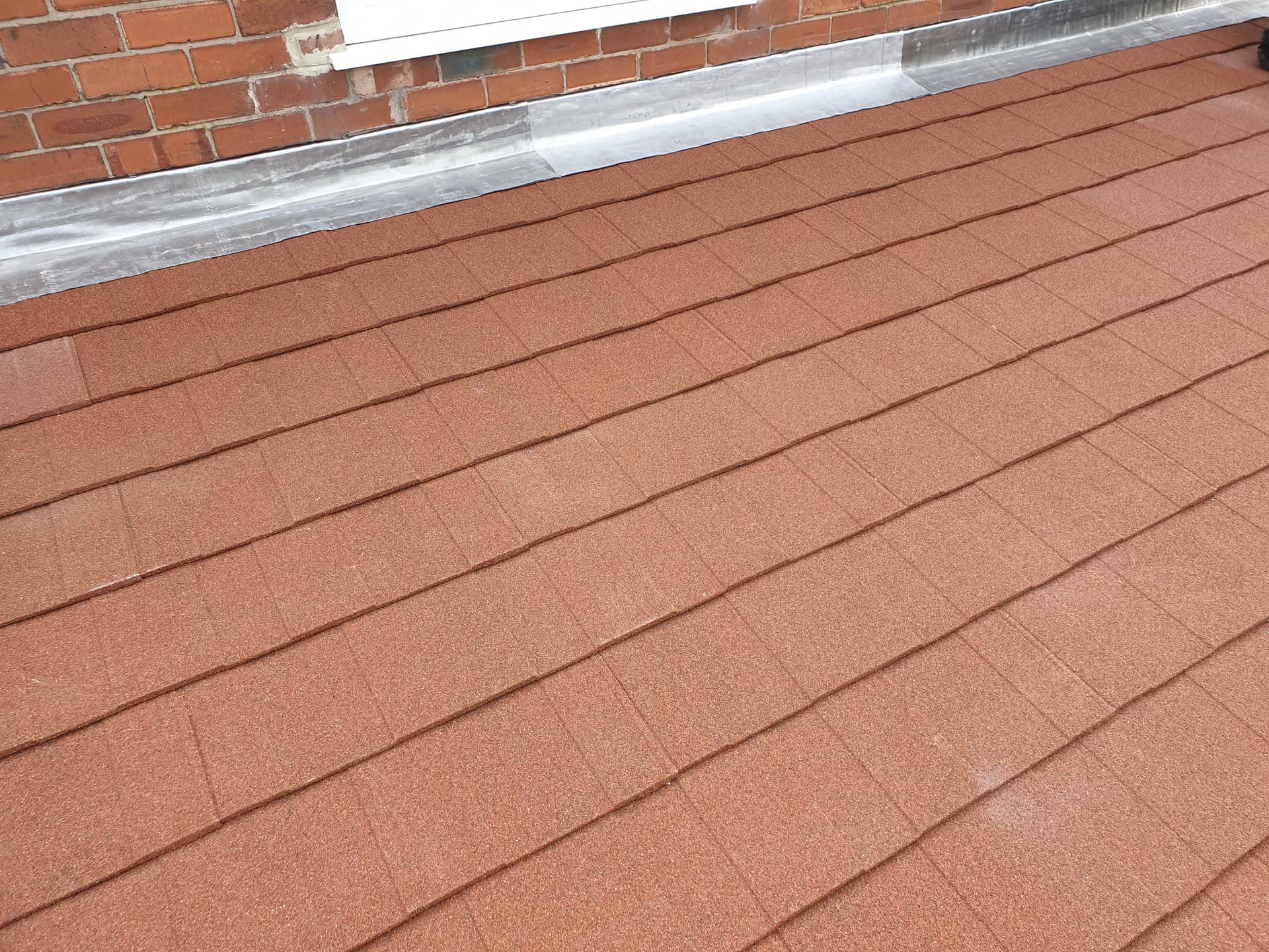 Pitched roof with terracotta concrete tiles and lead flashing against brick chimney