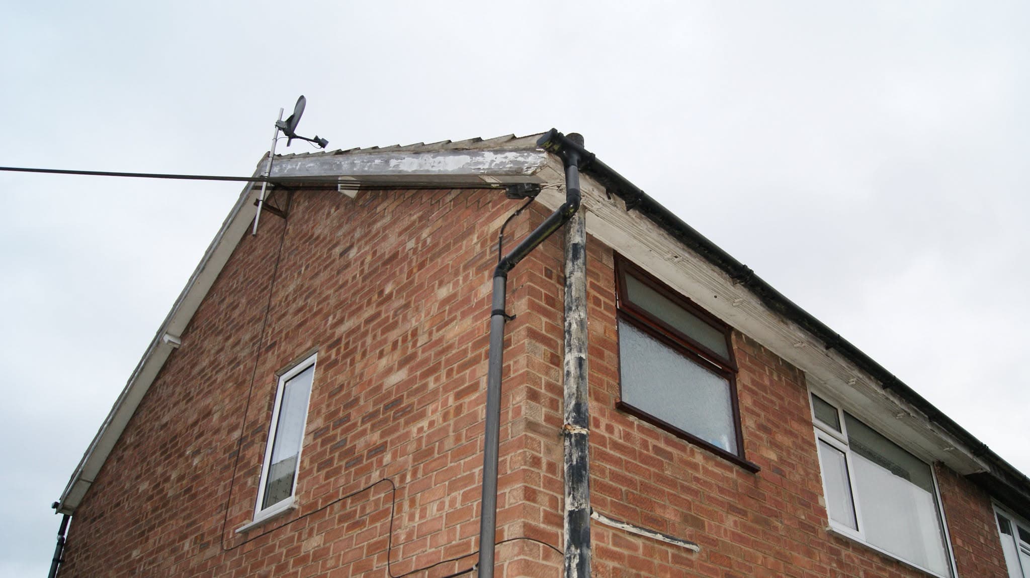 Pitched roof with damaged ridge tiles and fascias on brick gable end