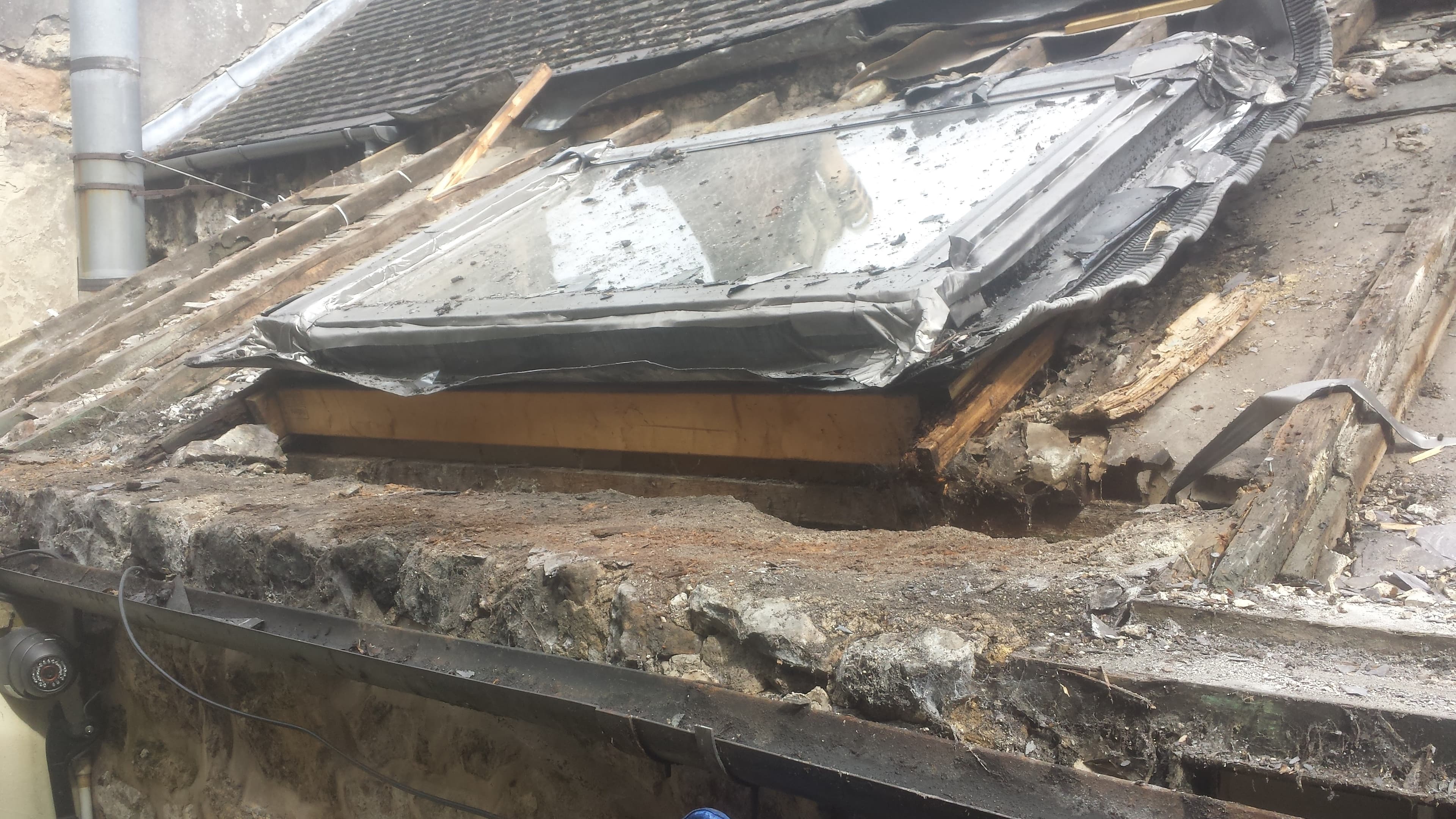 Damaged flat roof with torn felt and exposed timber decking during repair work