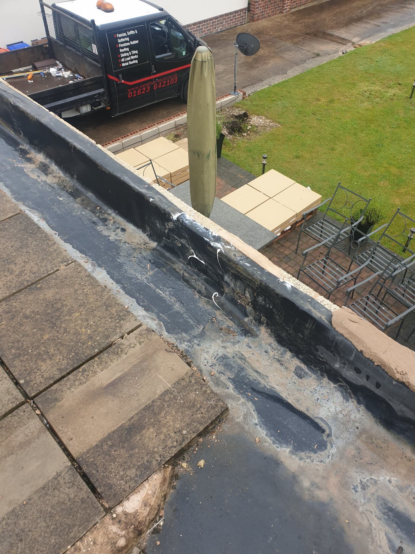 Flat roof with grey felt surface and company van parked below