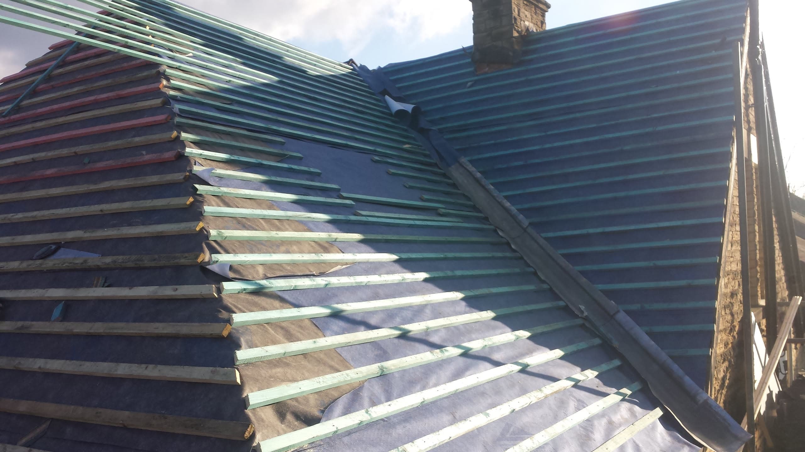 Pitched roof with dark grey concrete tiles being installed over battens and membrane