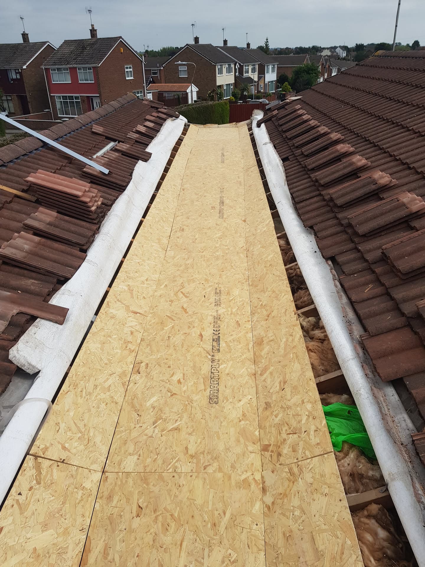 Pitched roof valley with new OSB boarding between brown concrete tiled roof sections