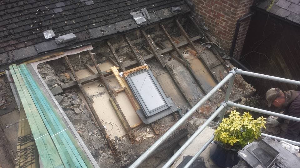 Flat roof stripped back to timber joists with skylight window and brick chimney visible