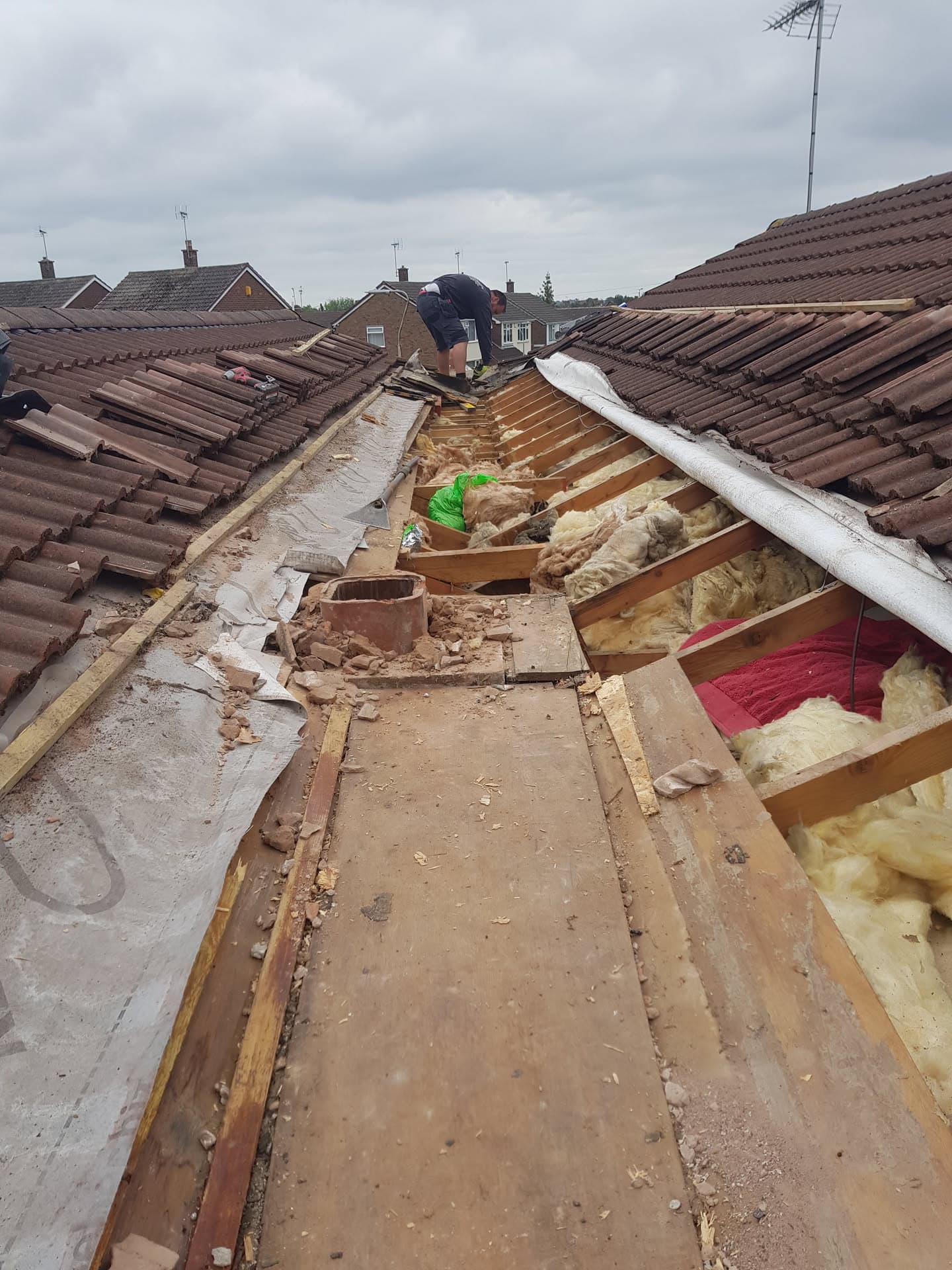 Fitter working on pitched roof repair with exposed timber rafters and insulation between brown concrete tiles