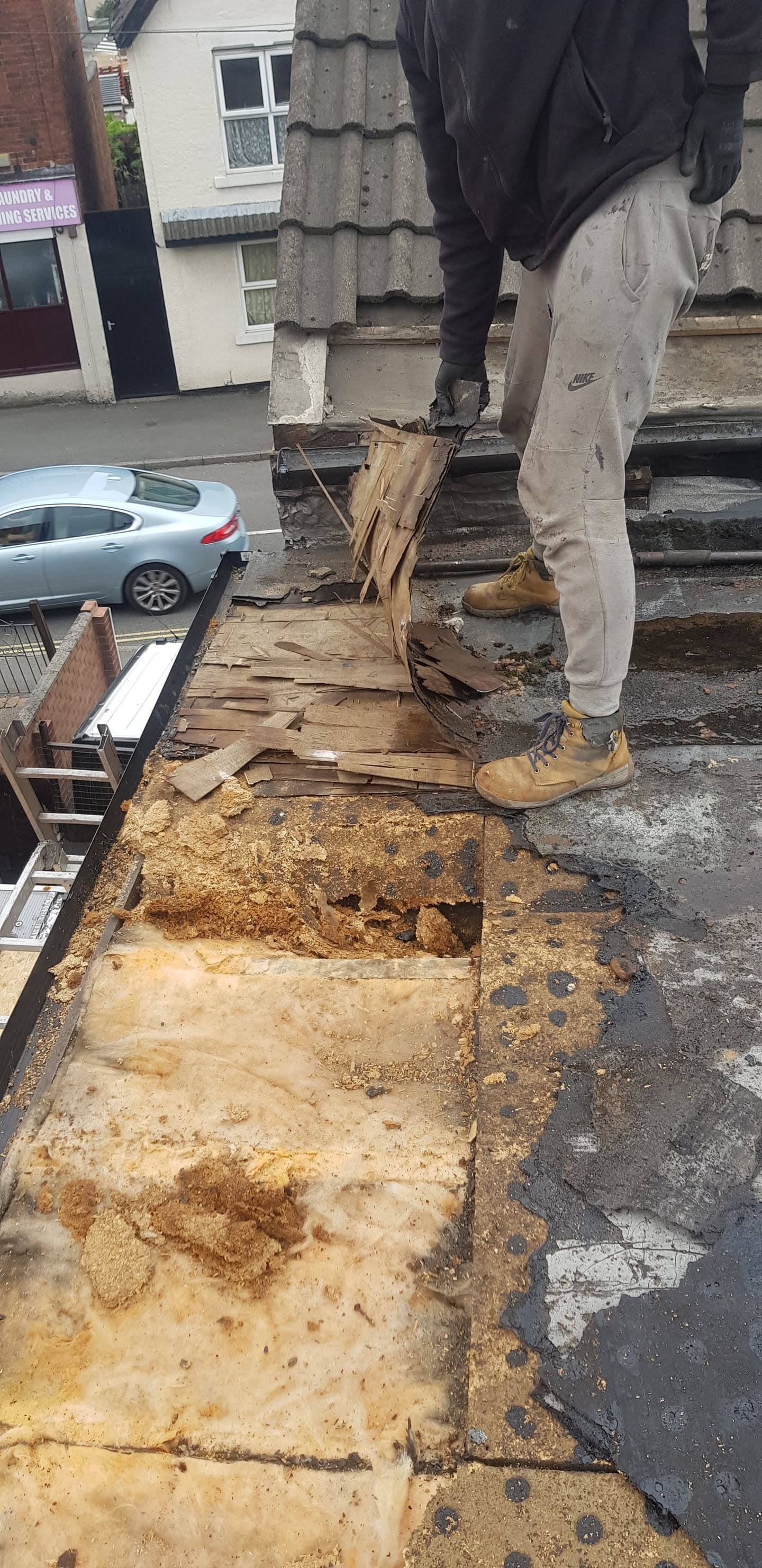 Roofer removing rotten timber and damaged felt from flat roof section