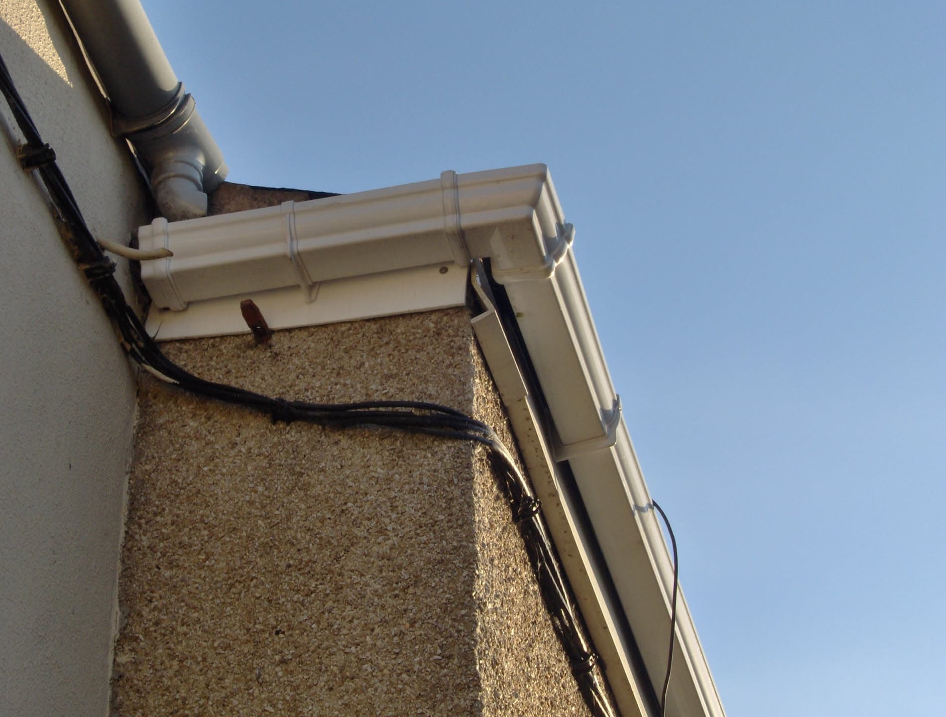 White fascia boards and guttering with downpipe on rendered wall