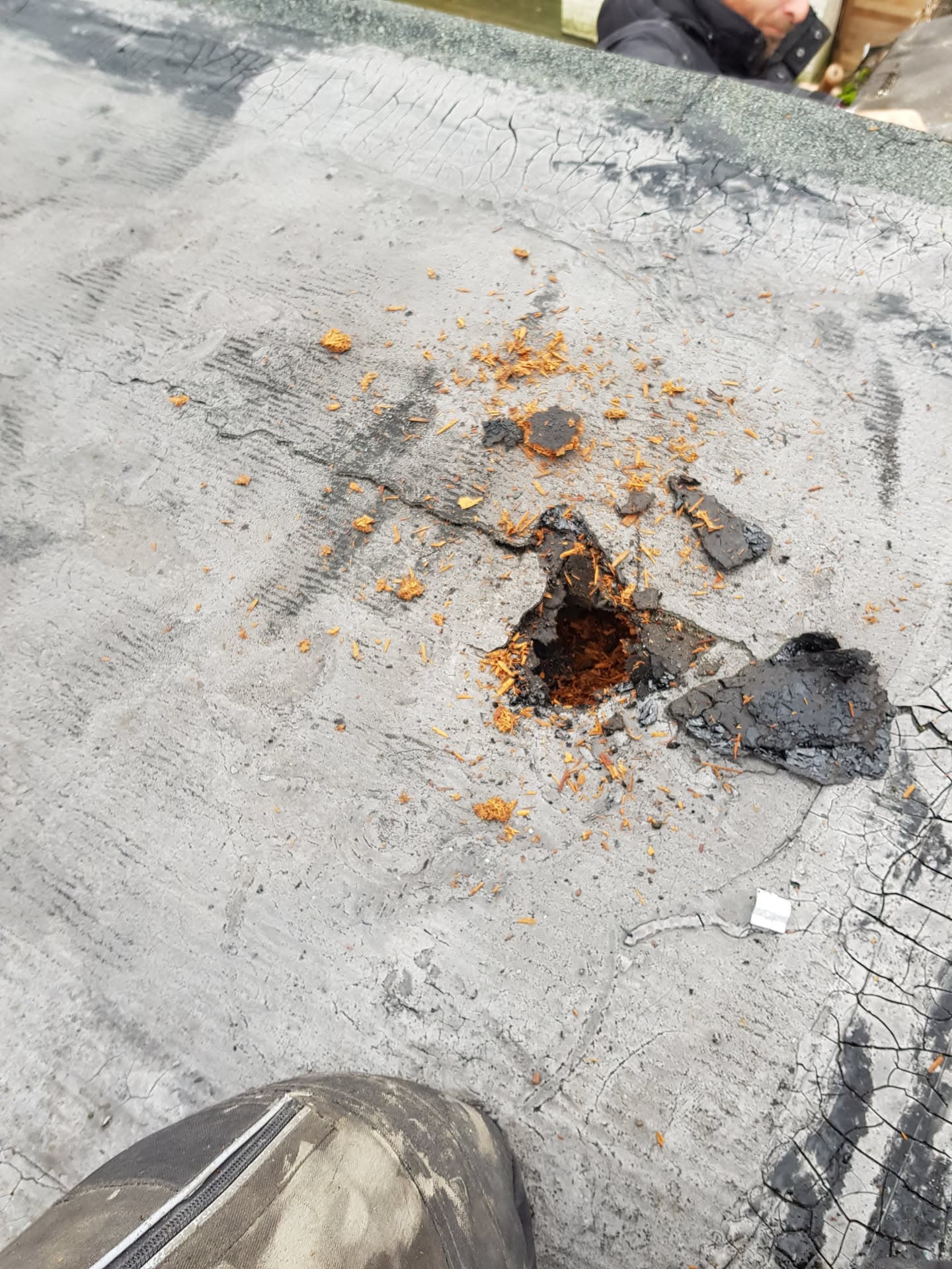 Damaged flat roof showing hole with rust staining and deteriorated felt surface