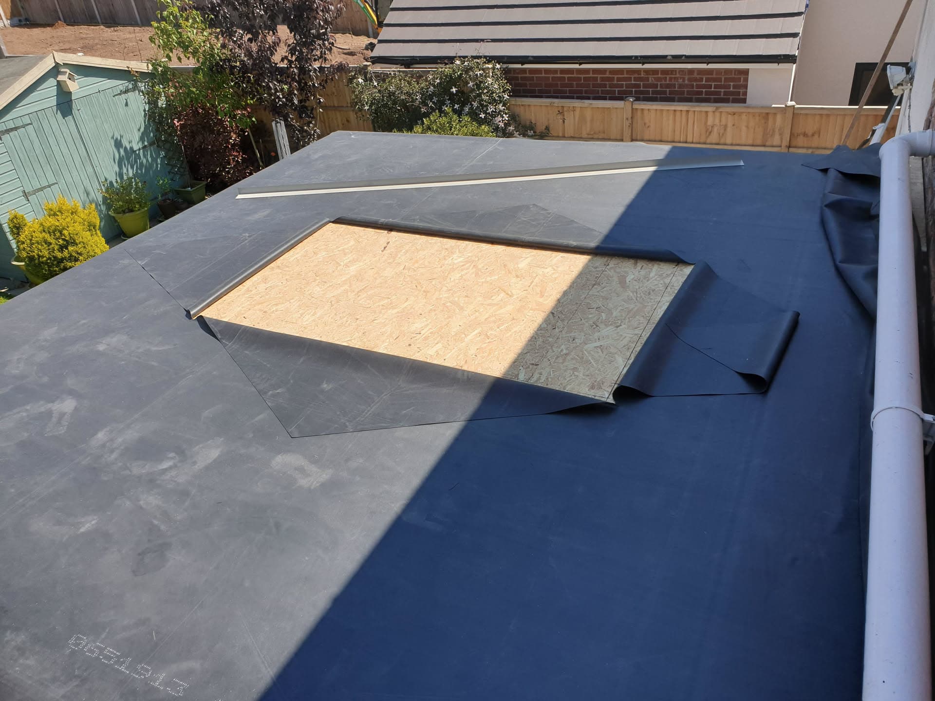 Flat roof installation in progress with grey EPDM rubber membrane and exposed plywood section
