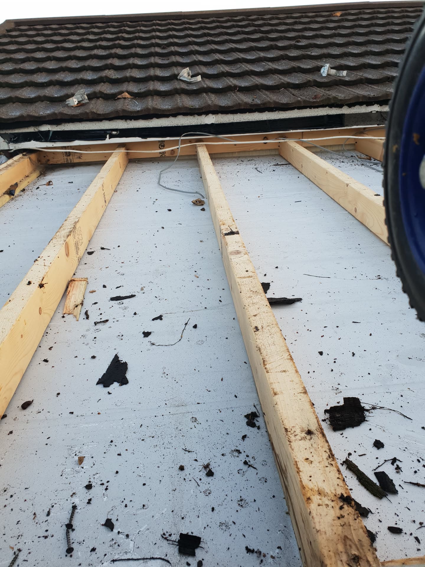 Flat roof with timber battens laid on grey felt membrane and dark concrete tiles visible above