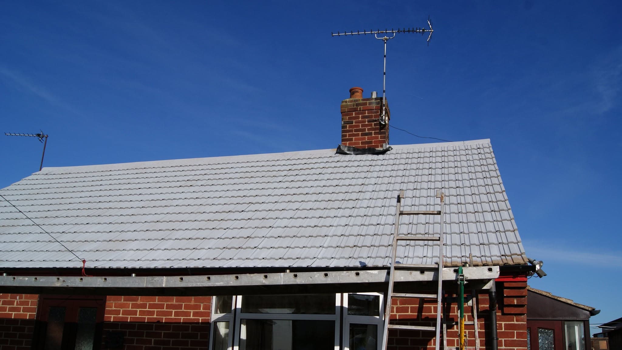 Pitched roof with light grey concrete tiles, brick chimney stack and TV aerial