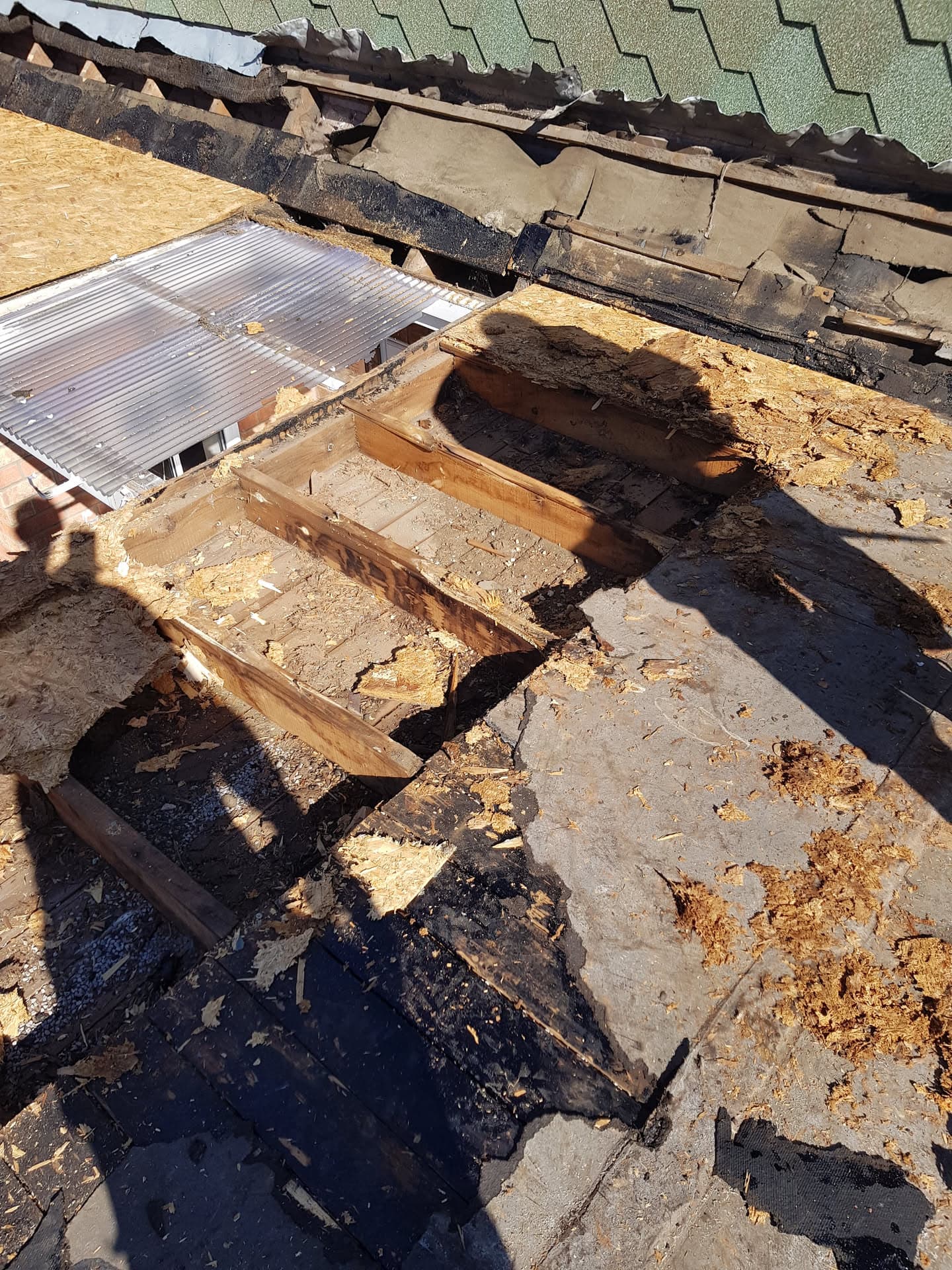 Damaged flat roof with exposed timber and deteriorated felt being prepared for repair