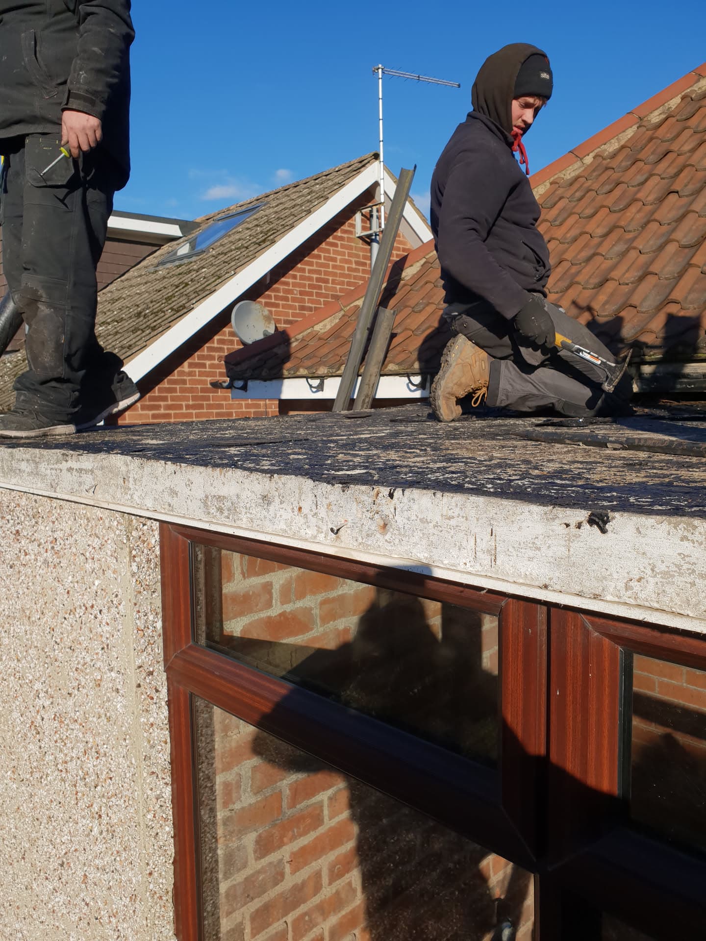 Roofer working on flat roof with red clay tiled pitched roofs visible behind