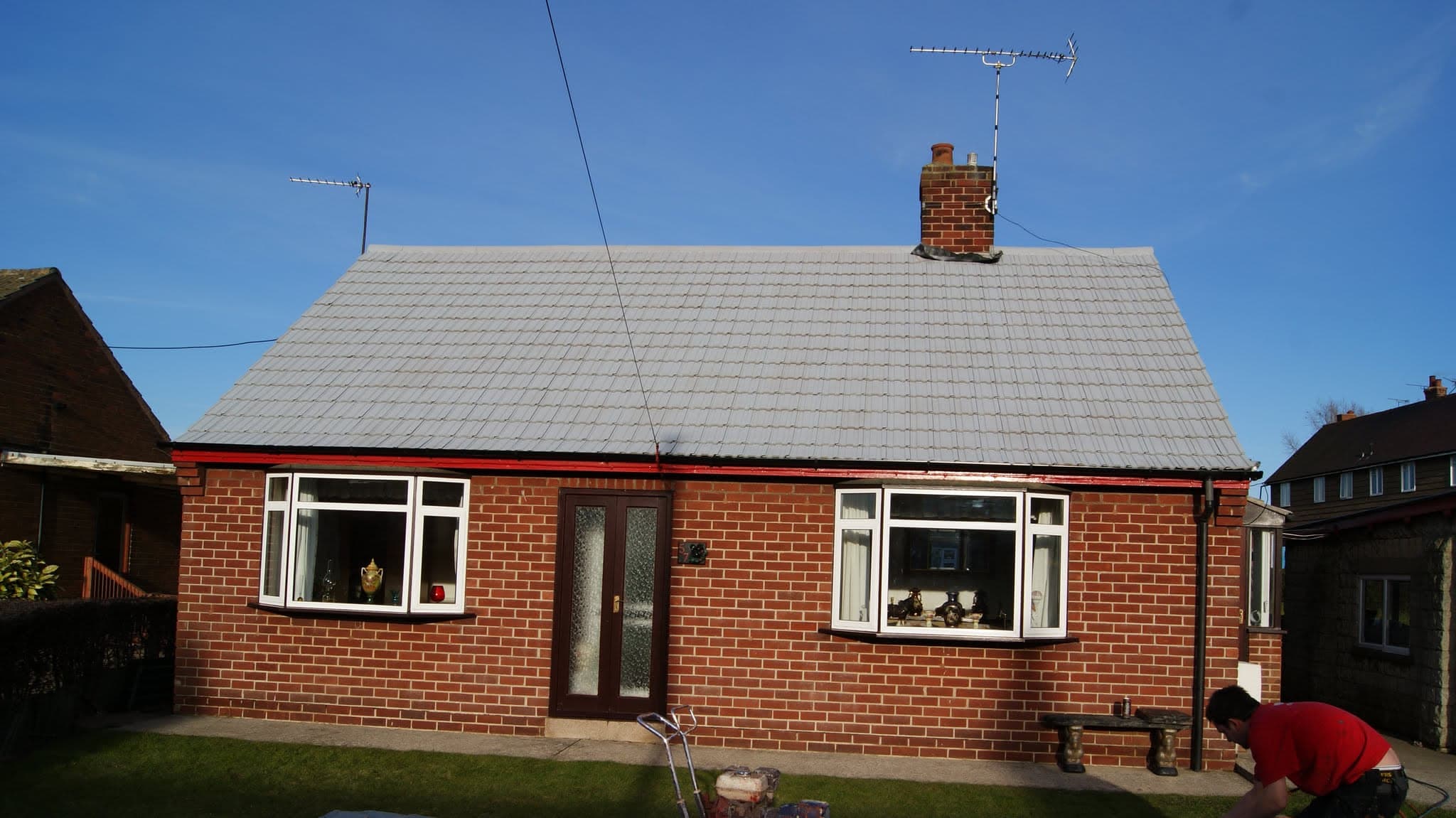 Pitched roof with grey concrete tiles and brick chimney stack on red brick bungalow