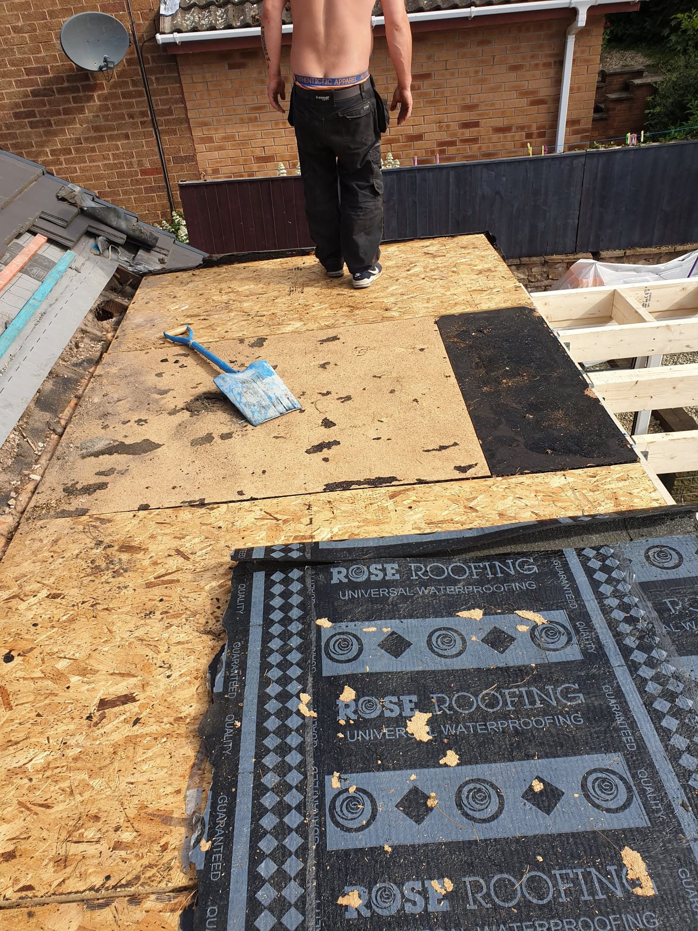Fitter standing on flat roof with OSB boarding and waterproof membrane during installation
