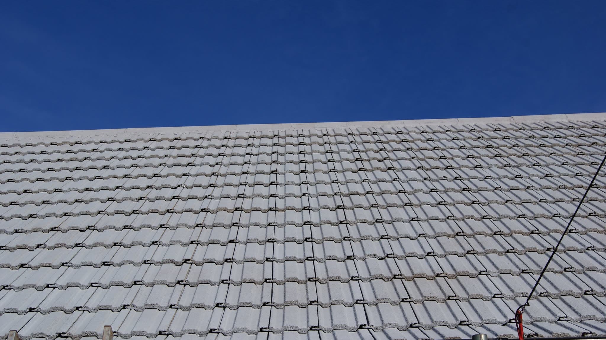 Pitched roof with grey concrete tiles against clear blue sky