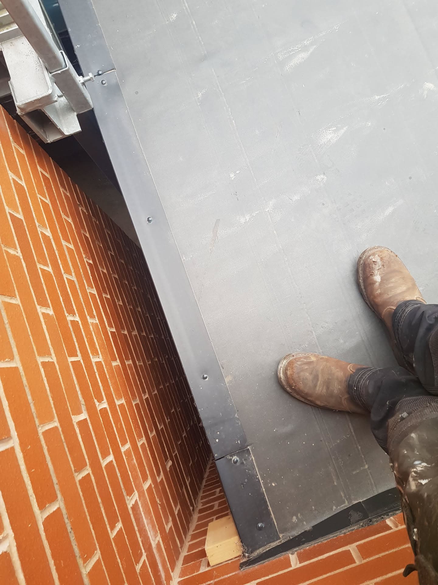 Grey GRP flat roof installation with metal trim against red brick wall