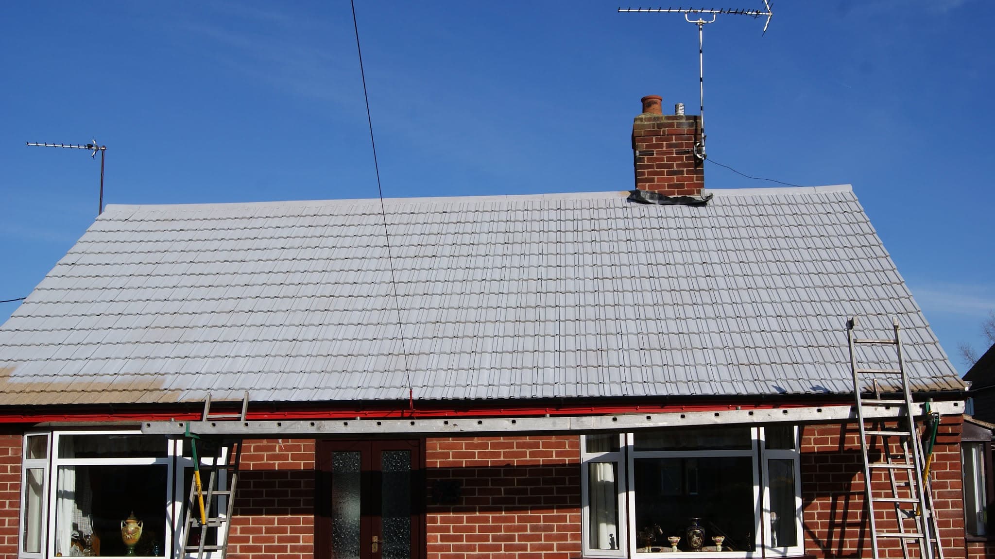Pitched roof with grey concrete tiles and brick chimney stack on red brick bungalow