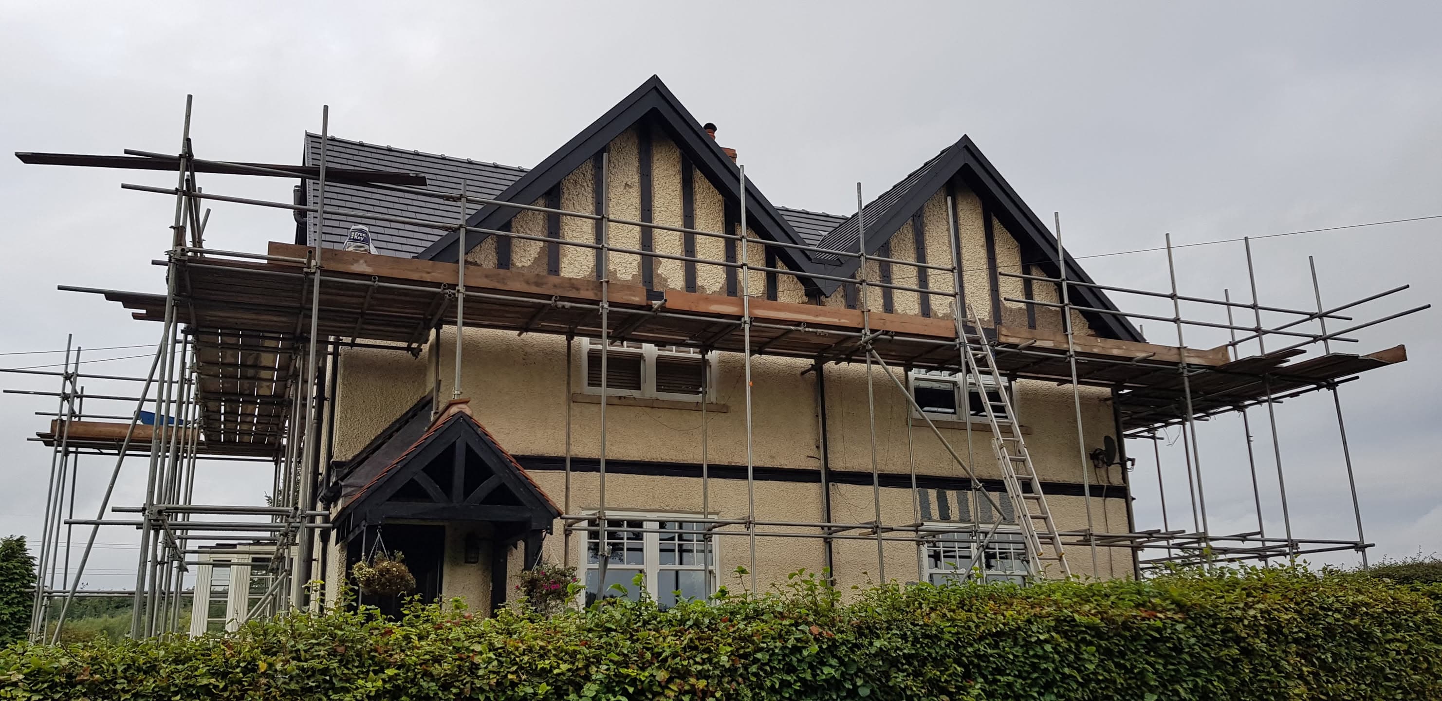 Pitched roof re-roofing in progress with dark tiles and scaffolding on detached house