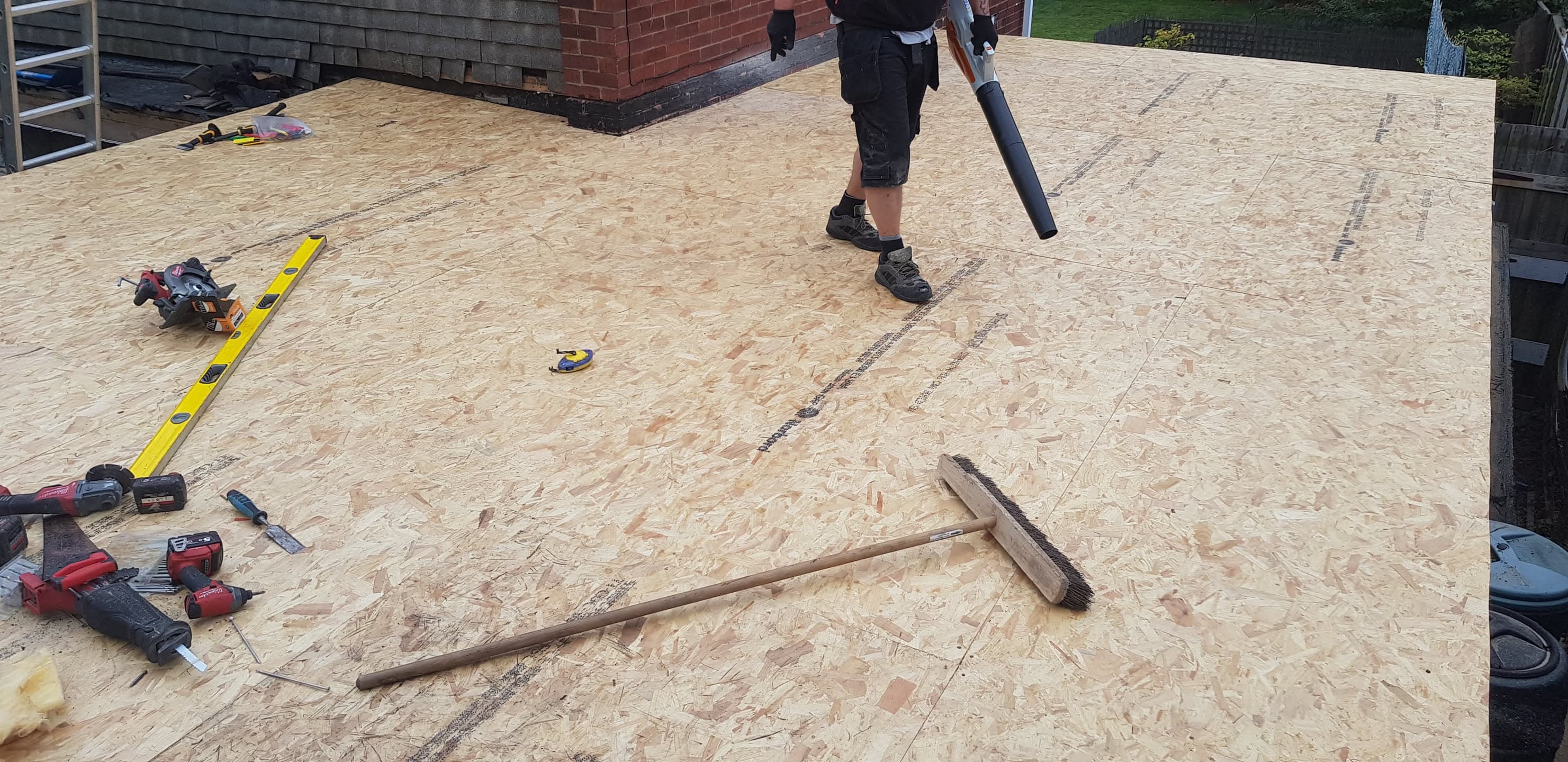 Fitter working on flat roof with OSB decking and tools visible