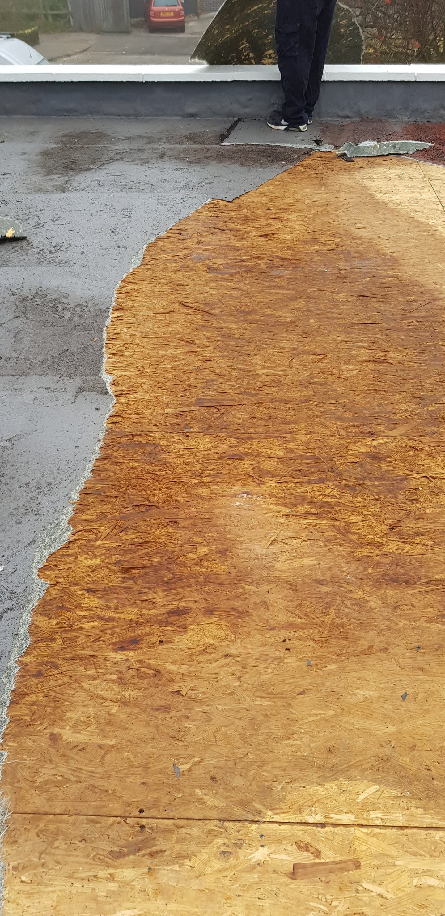 Flat roof installation showing OSB boarding and grey felt membrane with fitter standing on completed section