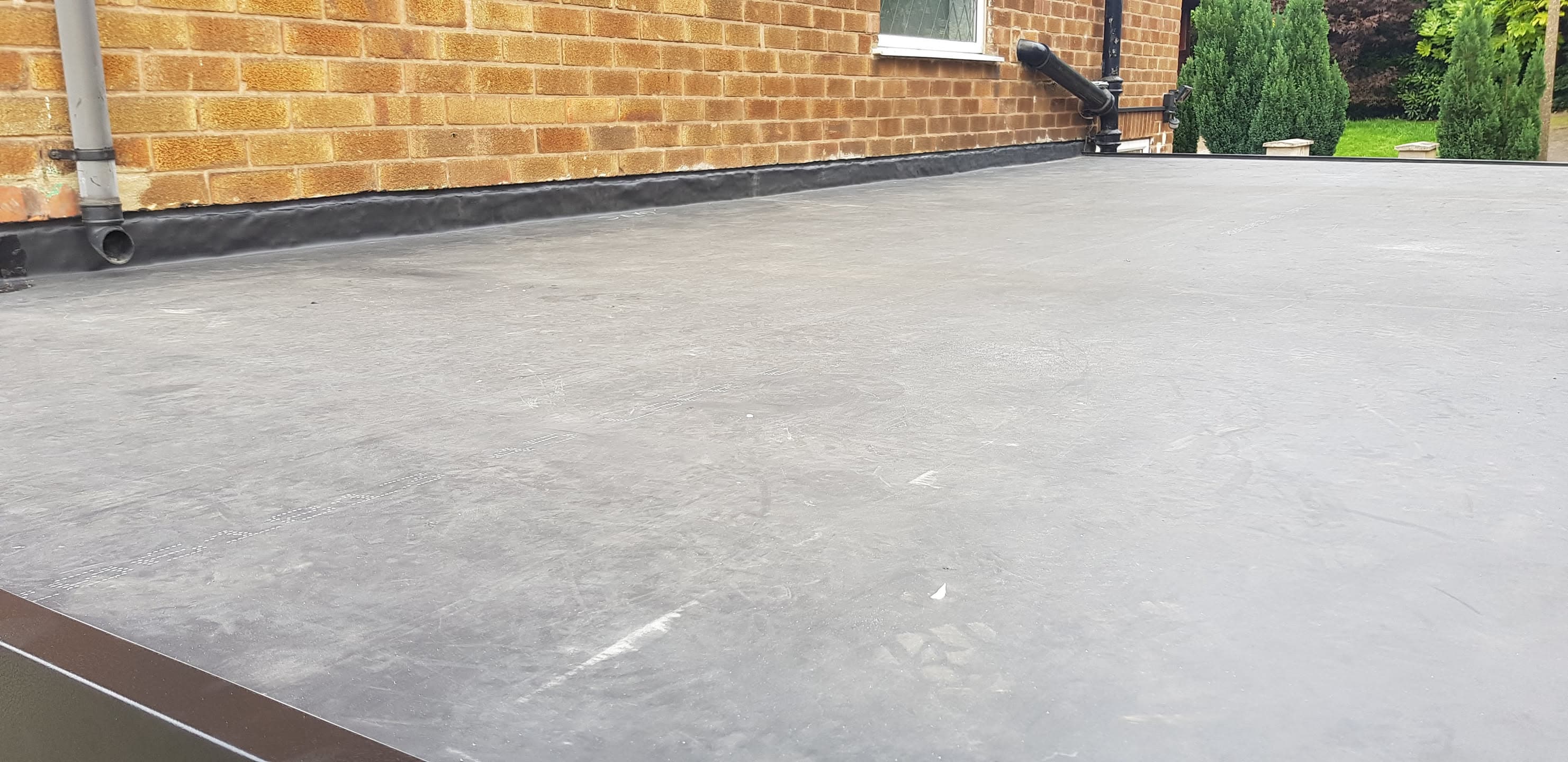 Completed grey EPDM rubber flat roof installation with black flashing against brick wall