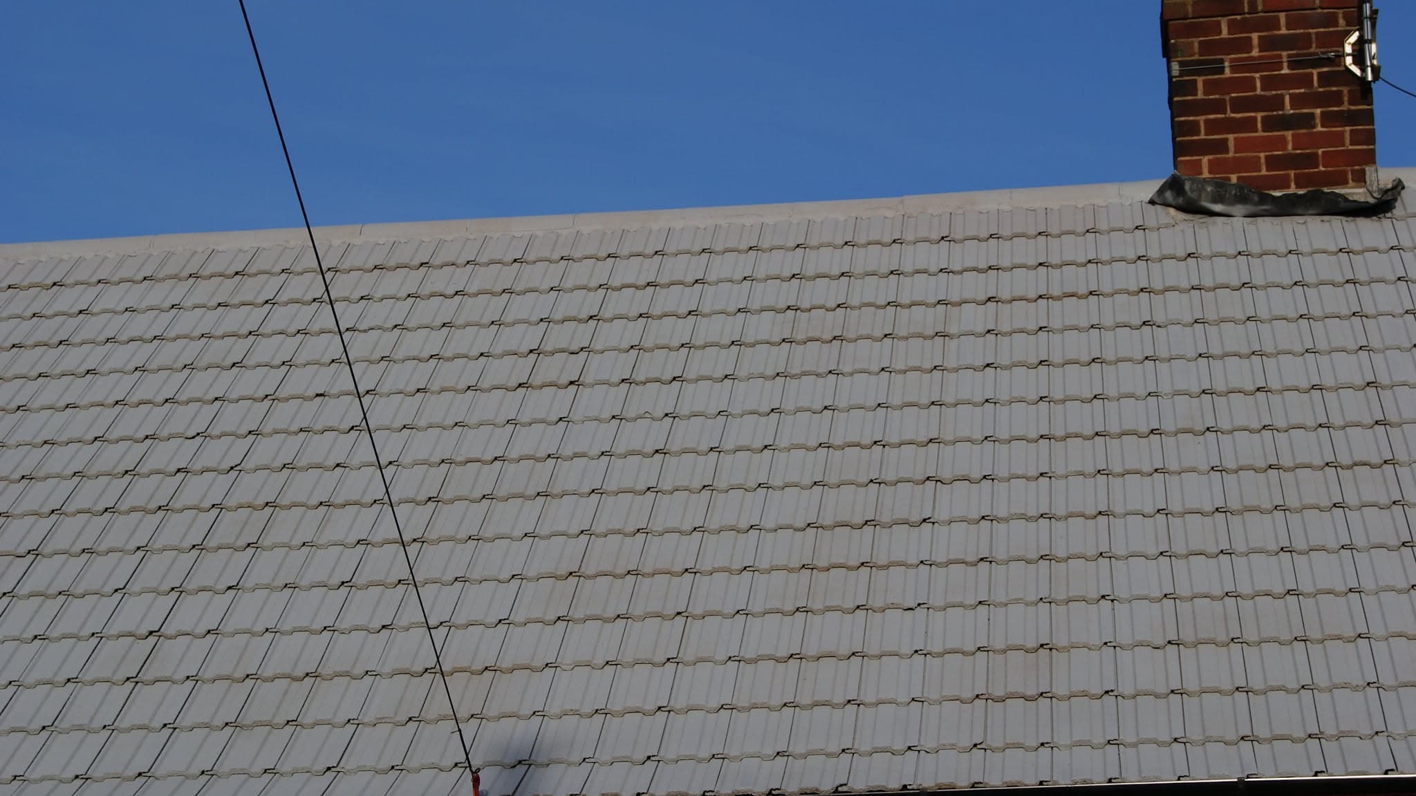 Pitched roof with grey concrete tiles and brick chimney stack