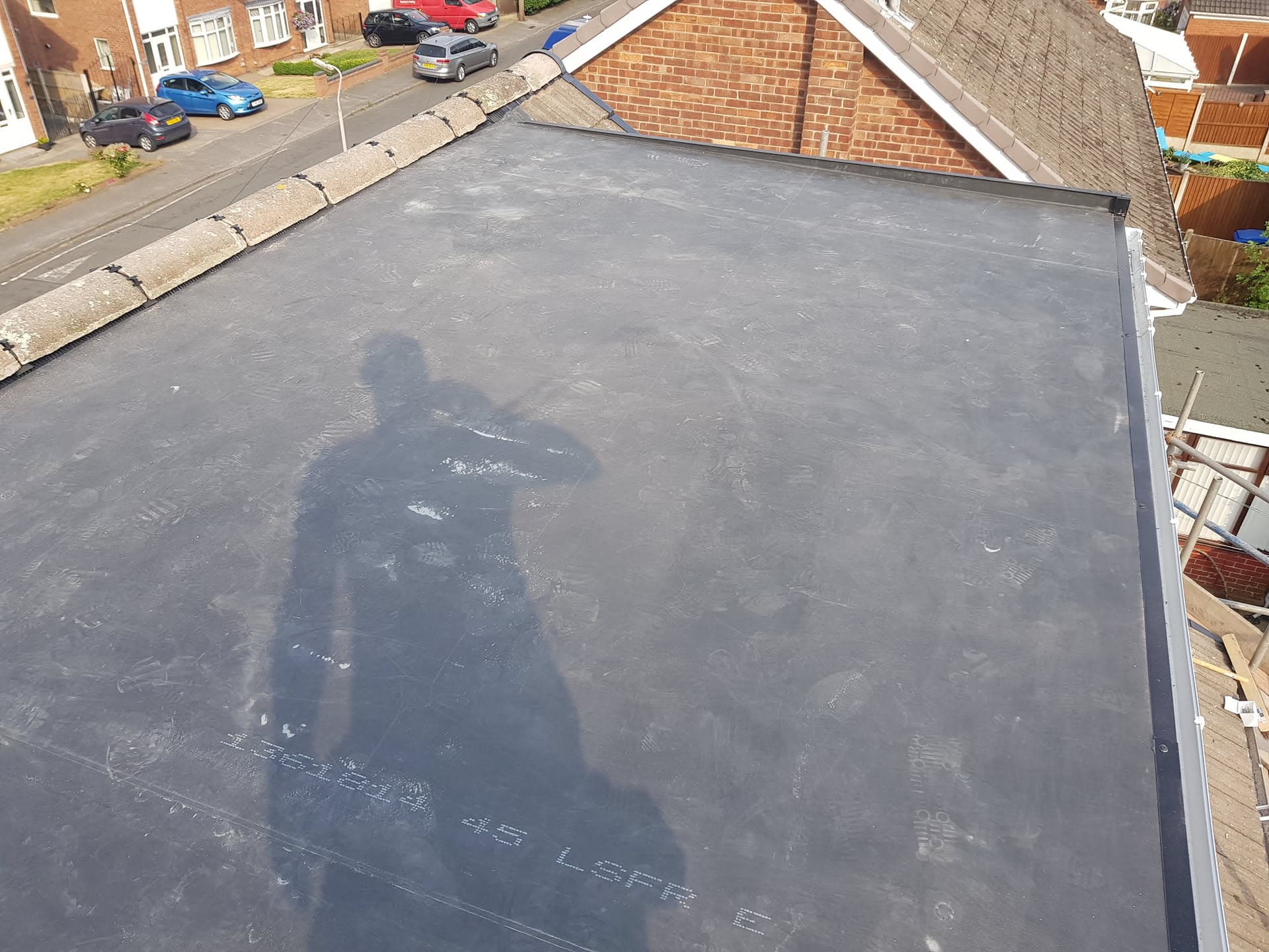 Flat roof with dark grey felt membrane on residential extension with tiled pitched roof visible